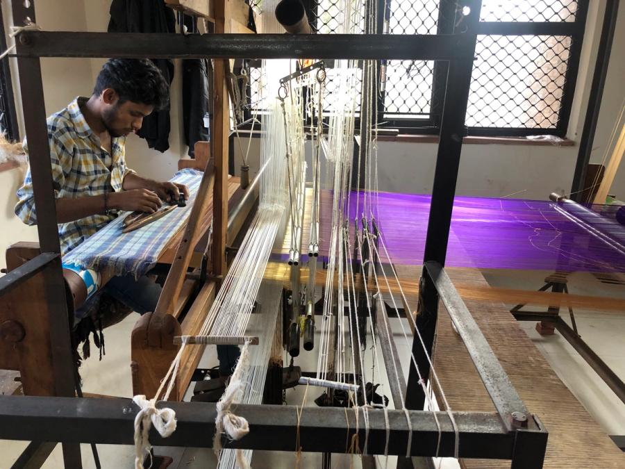 An Indian artisan working a traditional wooden handloom, weaving a Chanderi saree with purple thread