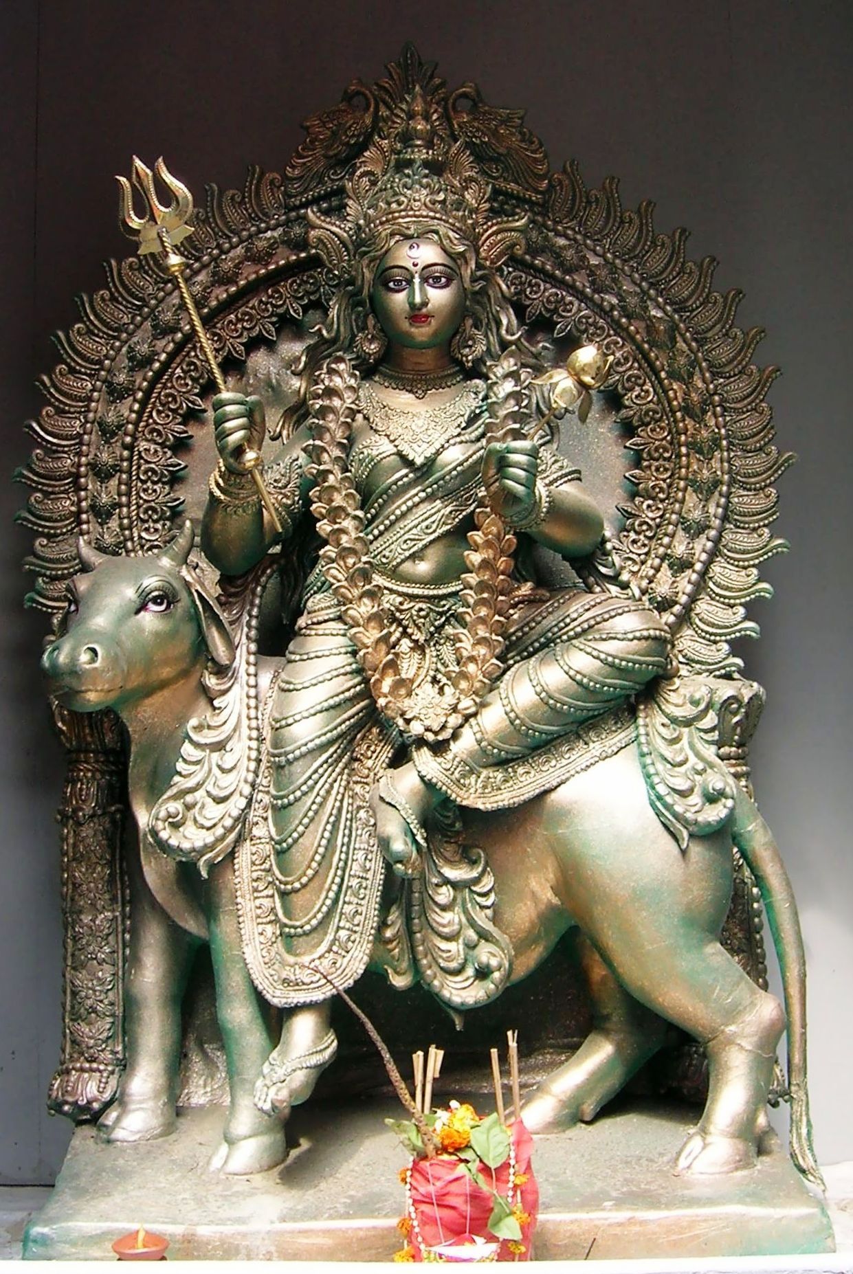 A silver-toned idol of Devi Shailaputri seated on her bull mount Nandi, holding a trishul in her right hand and a lotus in her left, worshipped during Durga Puja