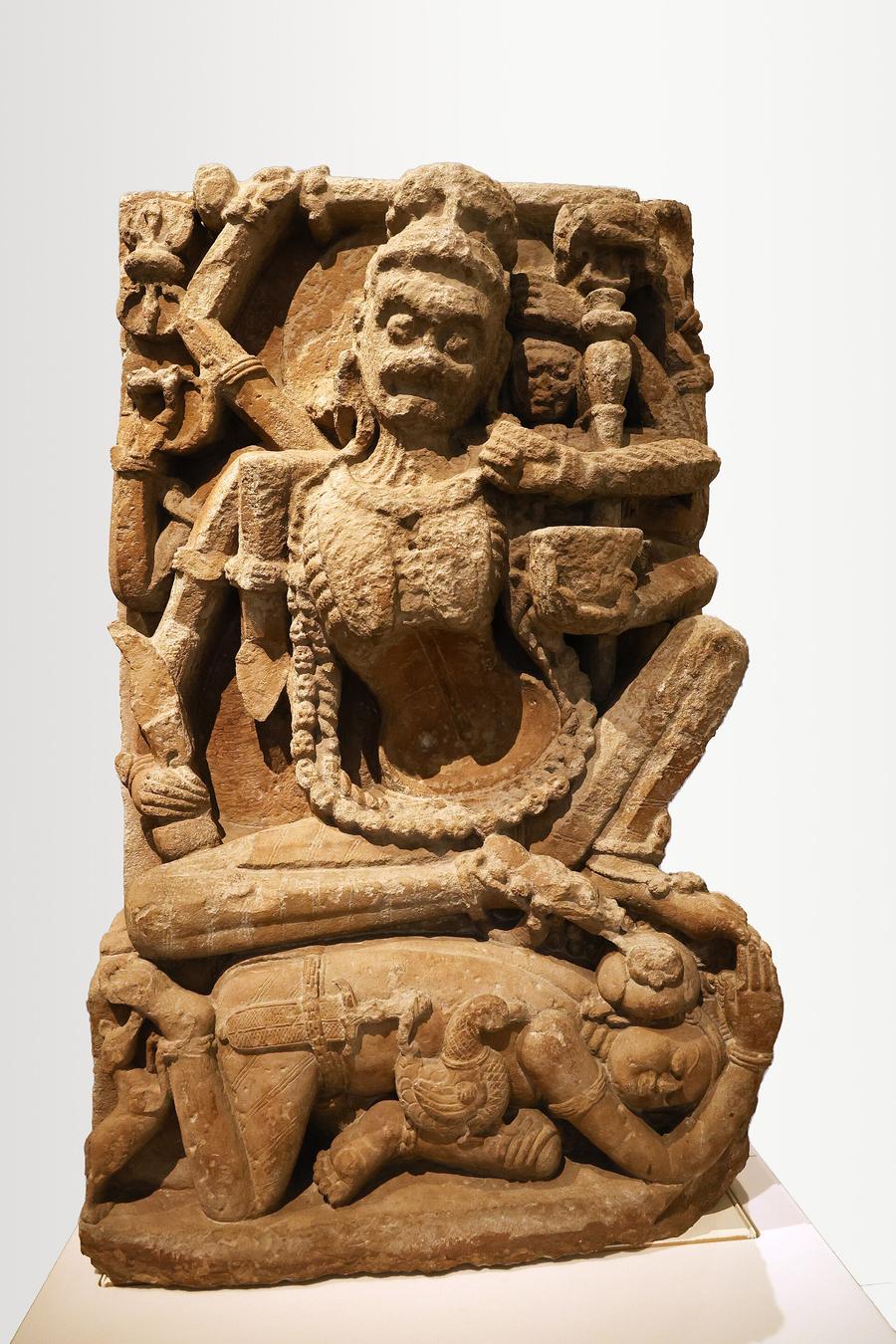 Ninth-century sandstone relief of the eight-armed goddess Chamunda, emaciated and skeletal, adorned with bone and skull ornaments, seated on a recumbent figure