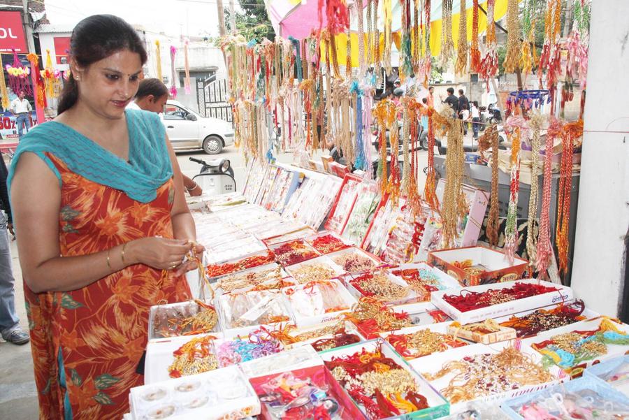 A woman shopping for rakhi threads at a market stall strung with colourful Raksha Bandhan bracelets