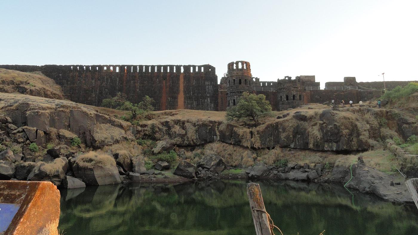 The ruined stone ramparts and bastions of Raigad Fort in Maharashtra, the hill fortress capital where Chhatrapati Shivaji Maharaj was crowned in 1674, reflected in a rock-cut water tank.