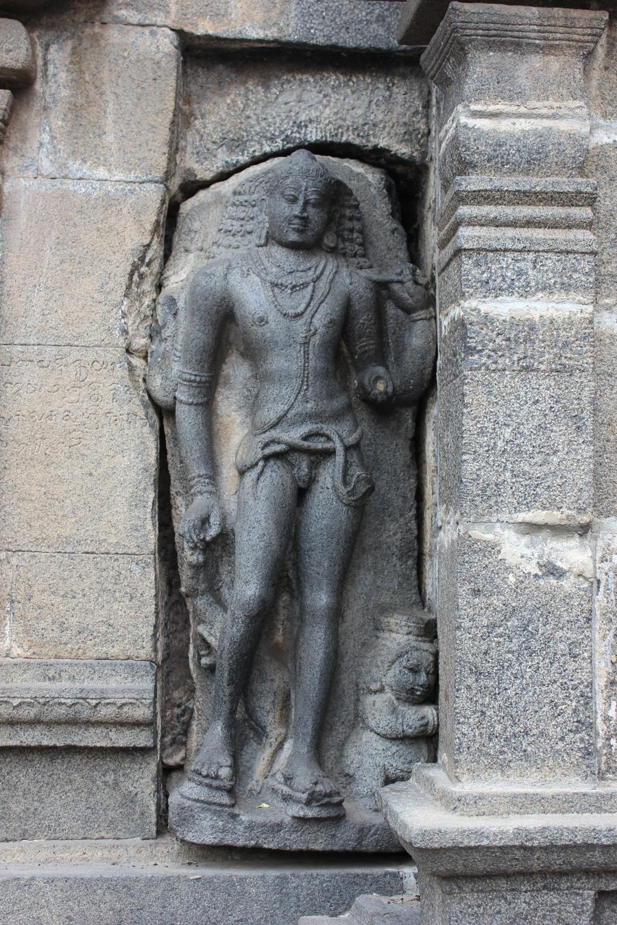 Stone sculpture of a nude standing ascetic form of Shiva with an animal at his feet.