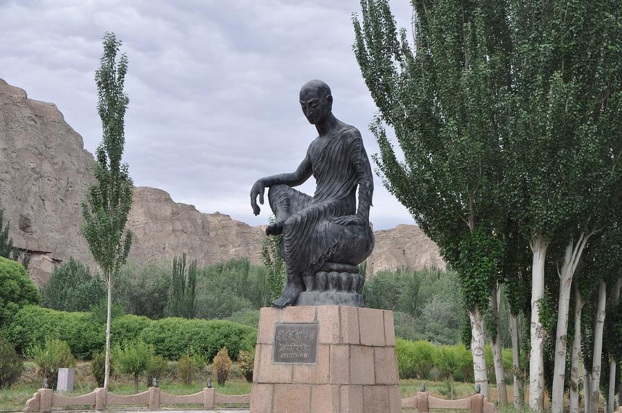 Bronze statue of the Buddhist monk and translator Kumarajiva seated on a lotus pedestal, with the cliffs of the Kizil Caves visible in the background near Kuqa, Xinjiang, China