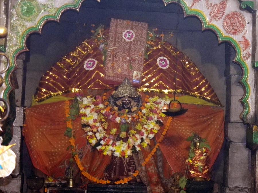 Garlanded dark stone murti of goddess Biraja enshrined under a decorated arch, Jajpur temple.