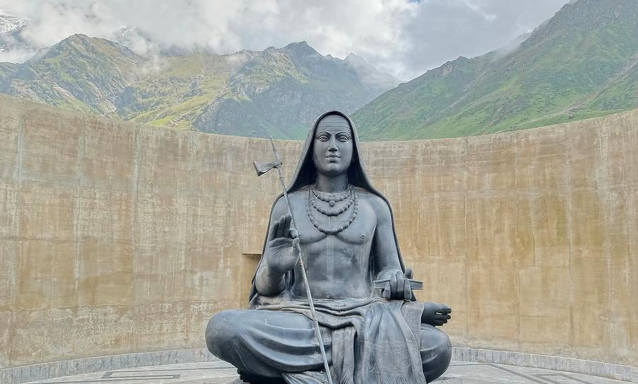 Statue of Adi Shankaracharya in meditation posture with the Himalayan peaks behind Kedarnath temple