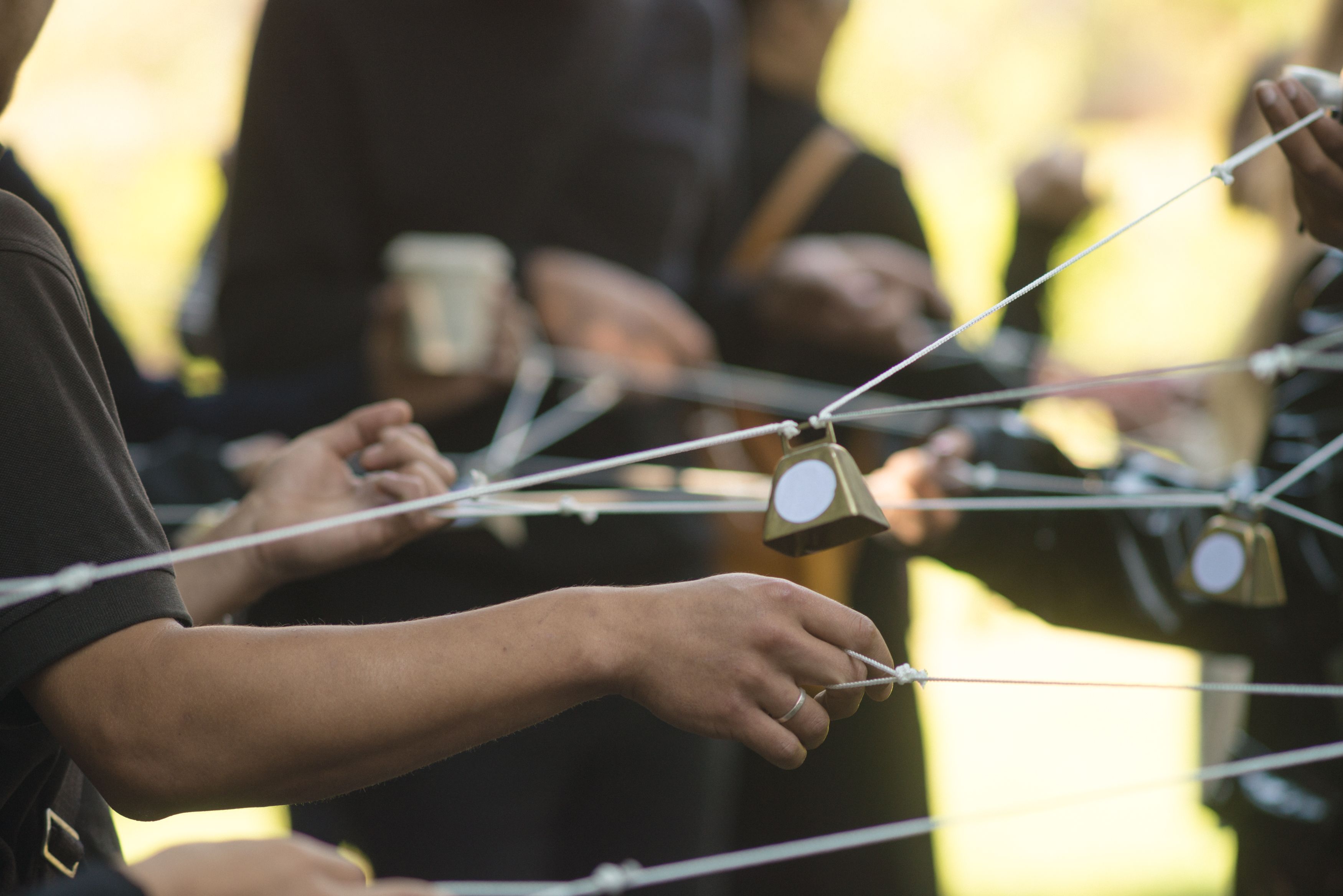 An image of a group of people whose fingers are joined by strings that allow them all to control the bells in-between