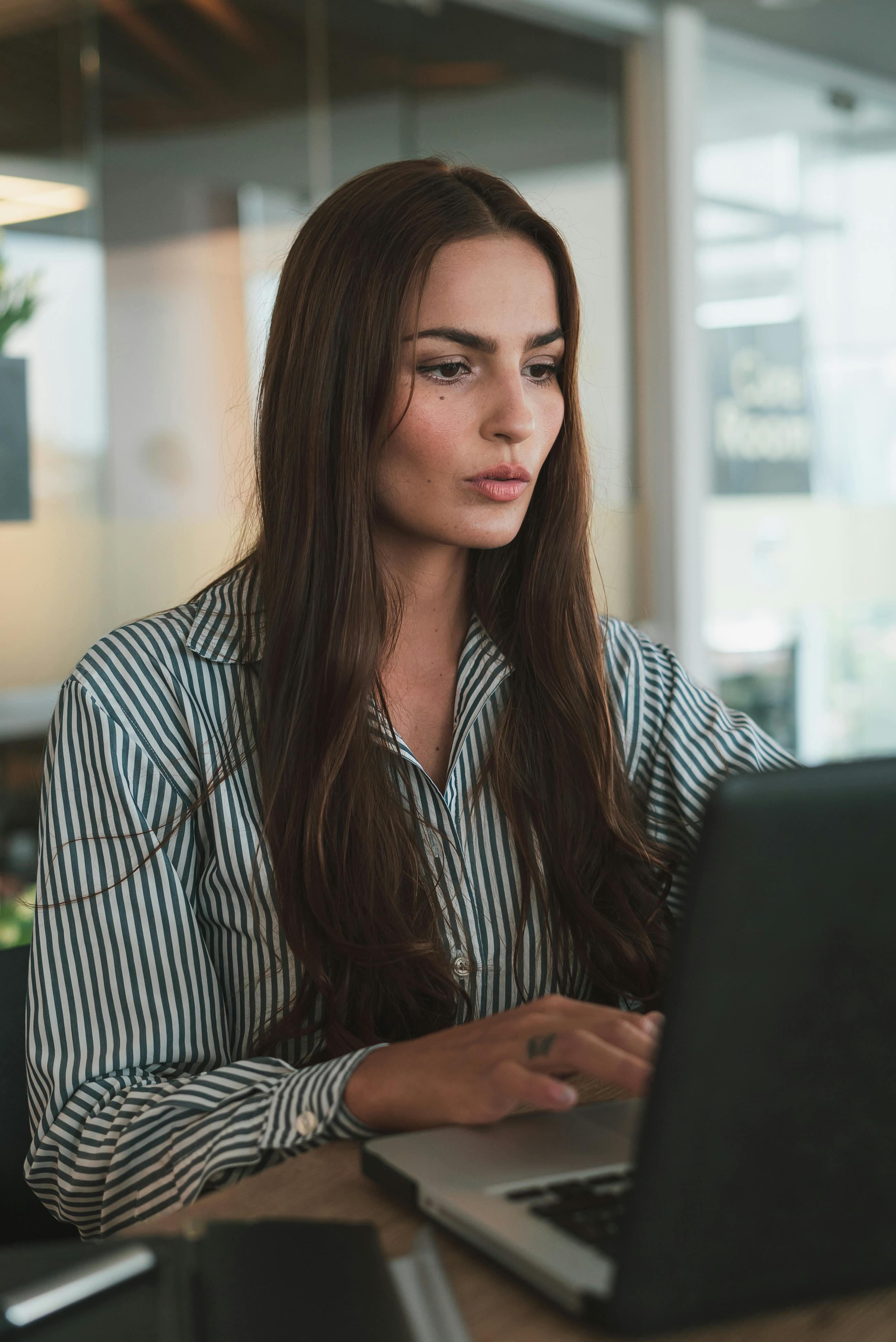 Woman with long hair sitting in front of laptop concentrating.