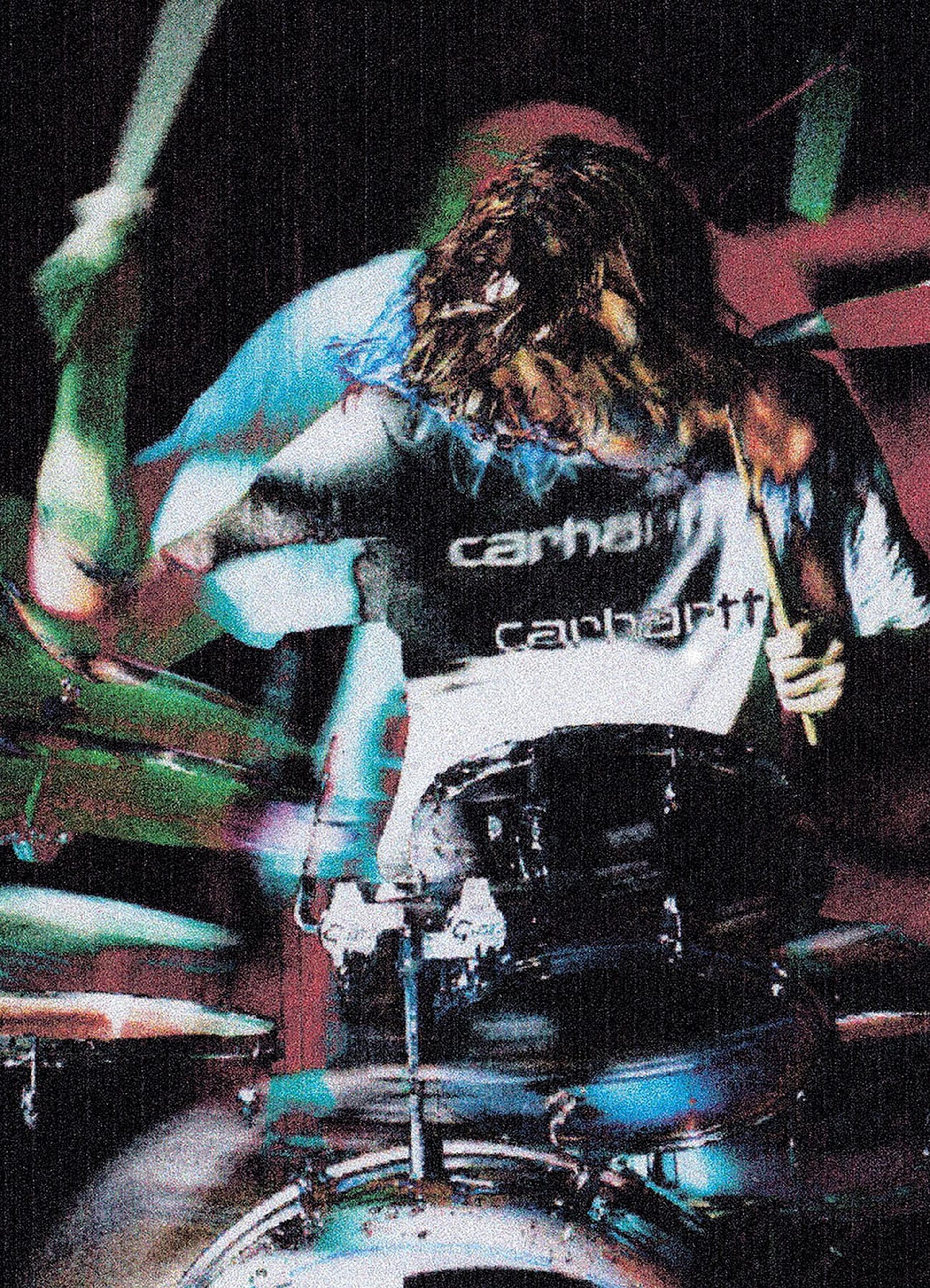 A motion-blurred drummer energetically plays a drum kit while wearing a Carhartt WIP T-shirt in a grainy, high-contrast image.
