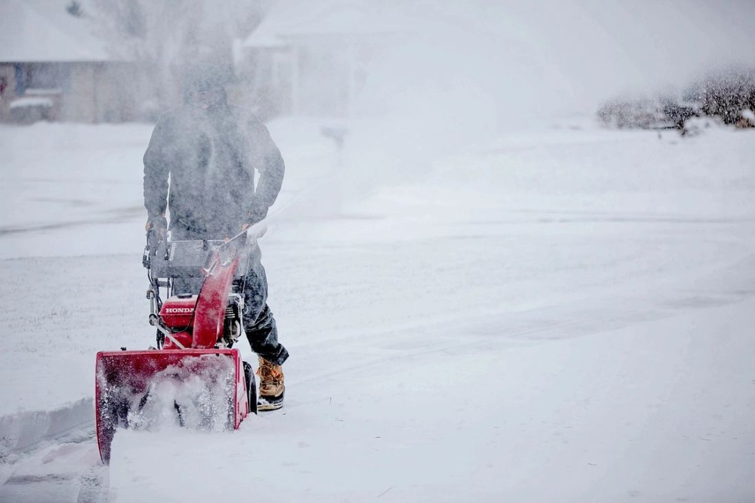 A worker clearing a driveway with a snow blower during heavy snowfall