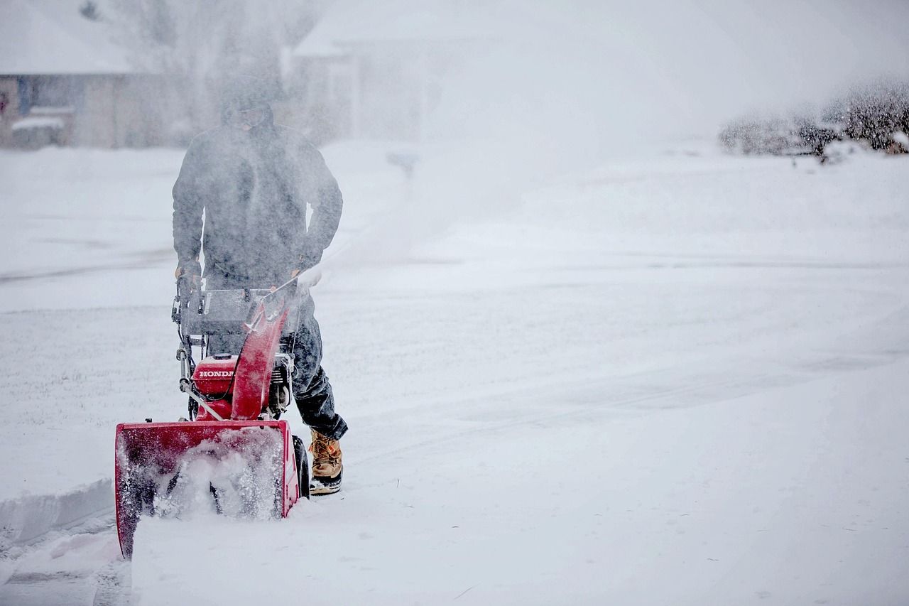 A worker clearing a driveway with a snow blower during heavy snowfall