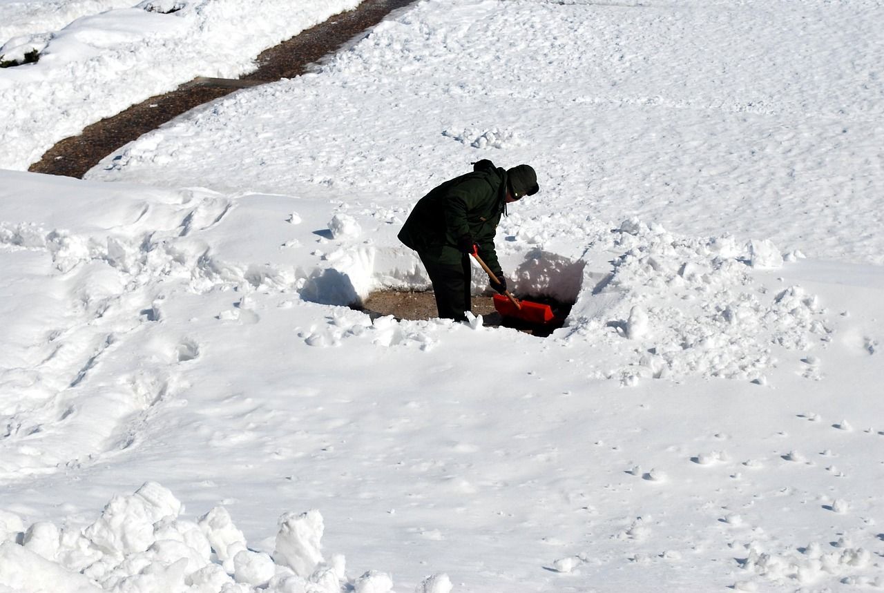 A person shoveling a path by hand through deep snow on a bright winter morning