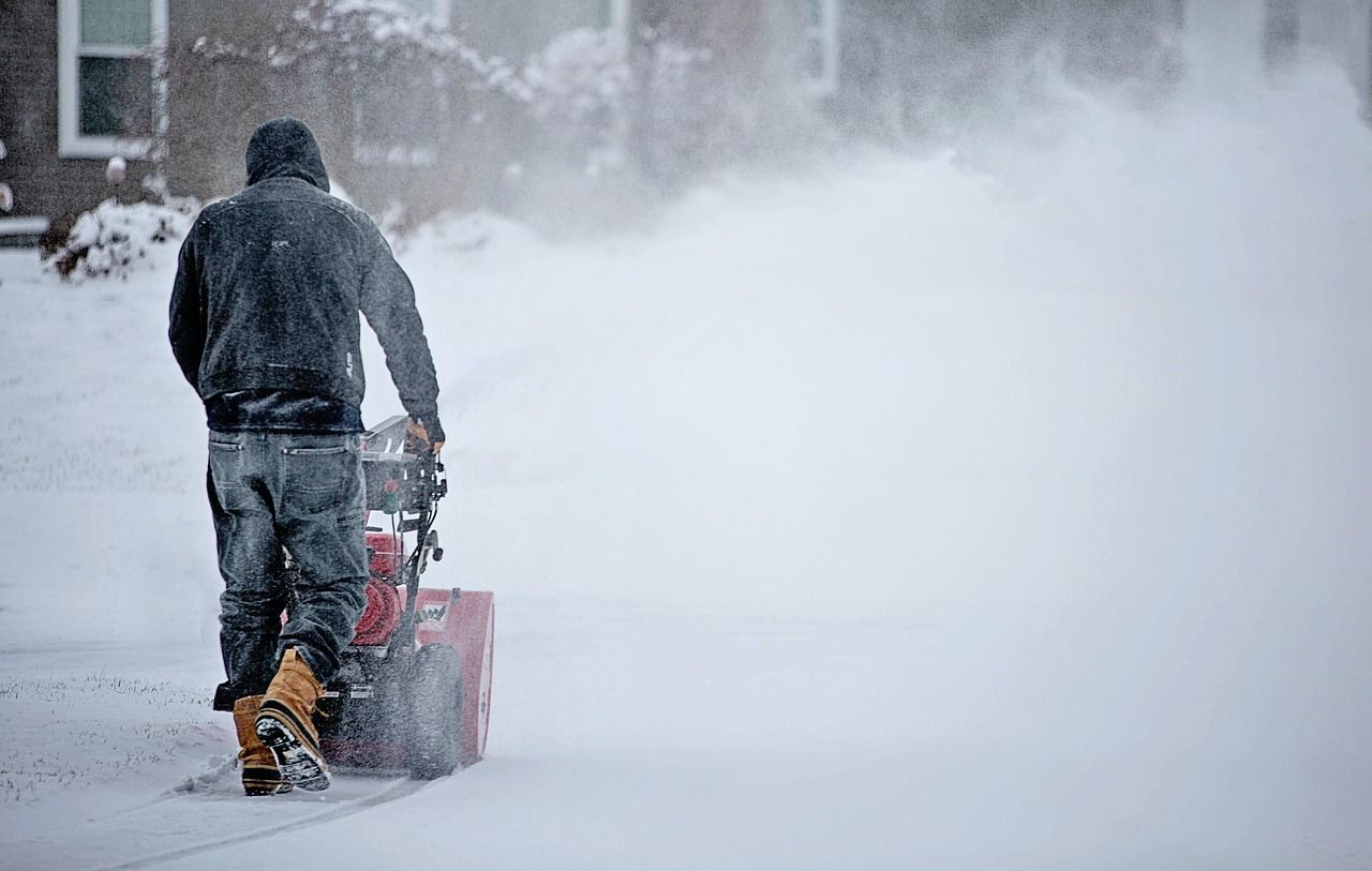 A worker seen from behind running a snowblower, throwing a wide plume of snow