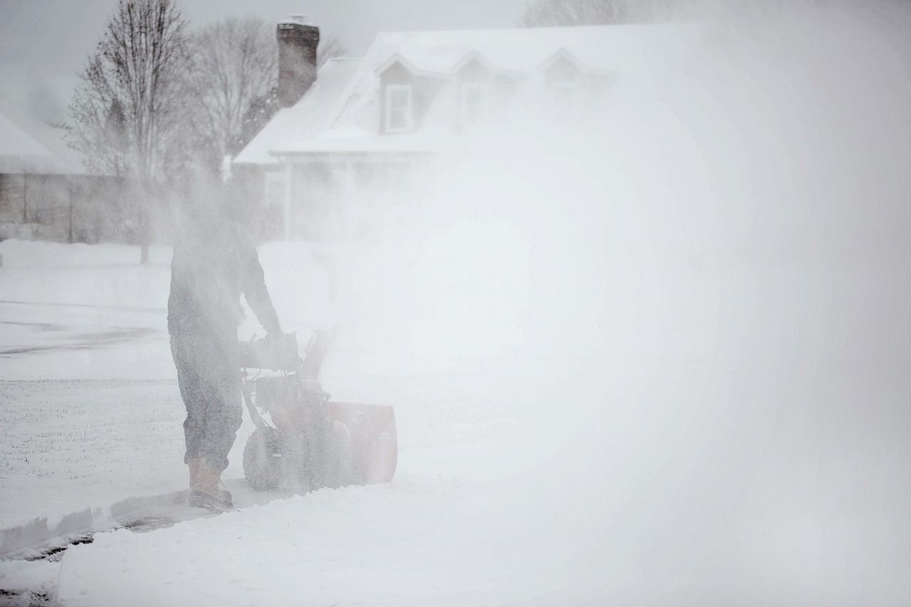A person running a snowblower down a driveway in front of a snow-covered house