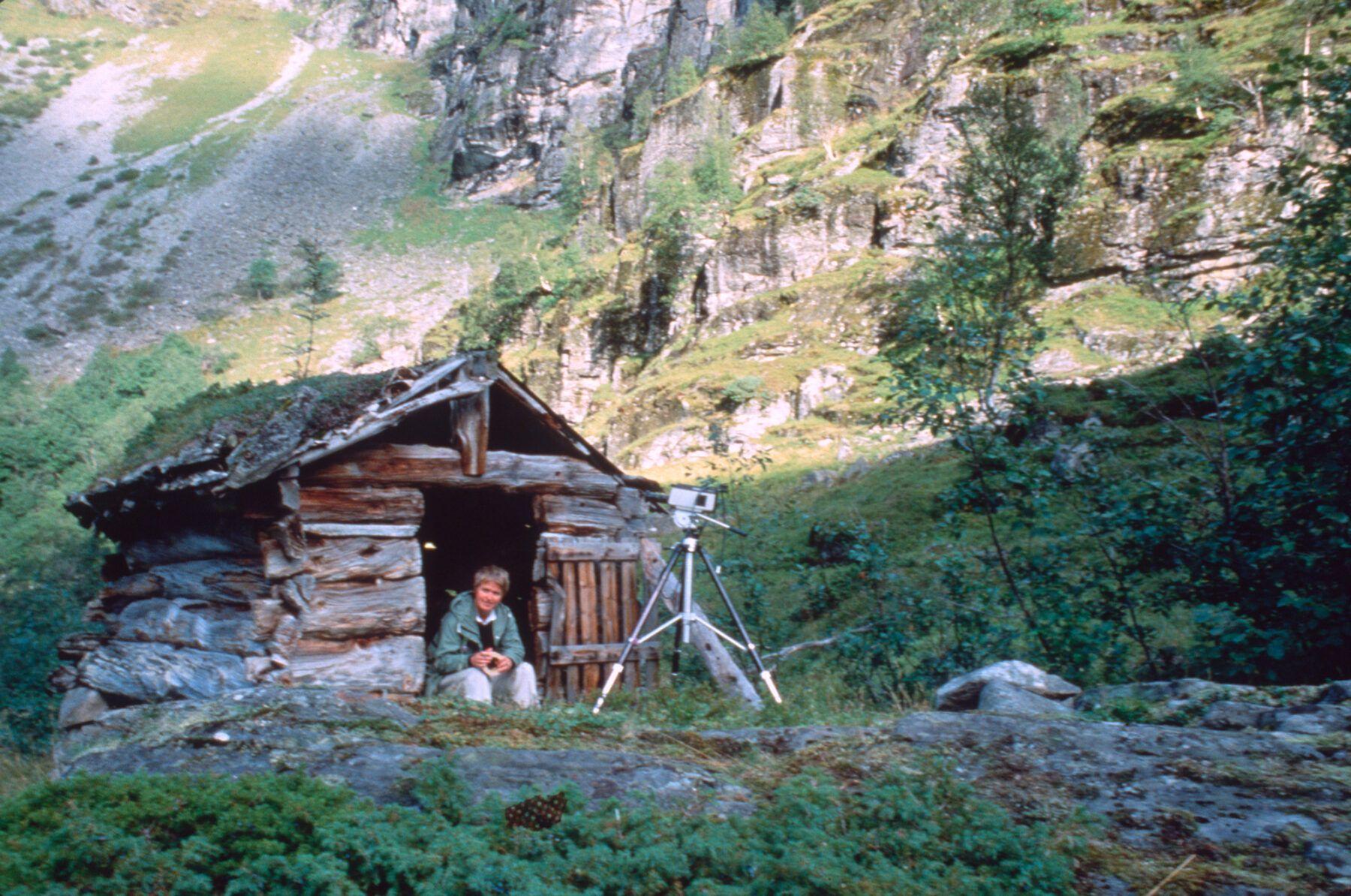 Kvinne sitter i døra til en liten hytte i fjellet