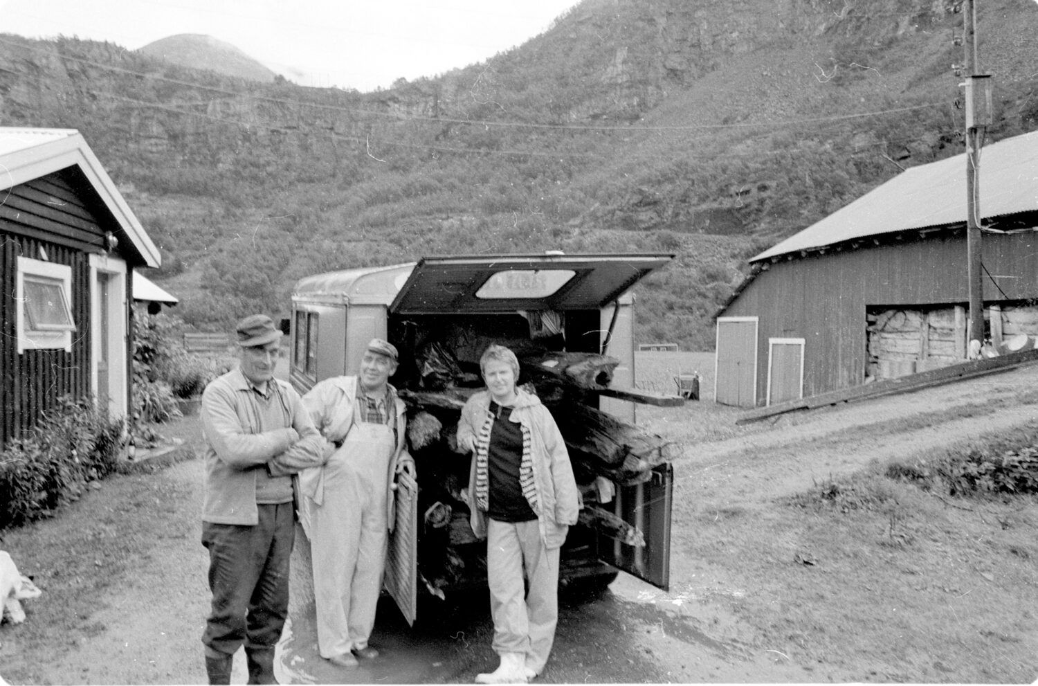 Svart/hvitt-foto av tre personer som står foran en bil pakket med planker