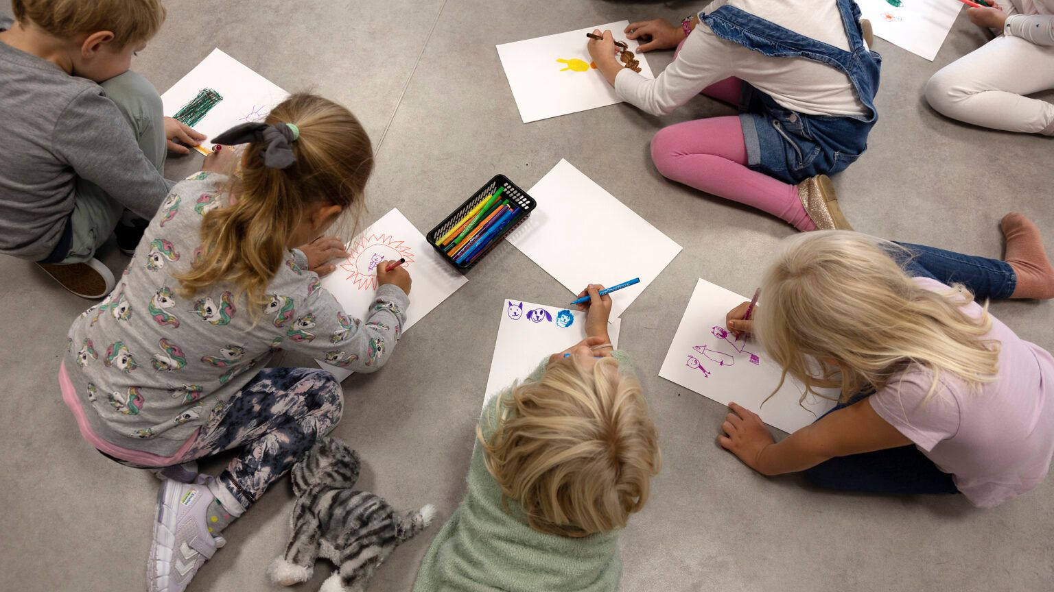Små barn tegner mens de sitter på gulvet
