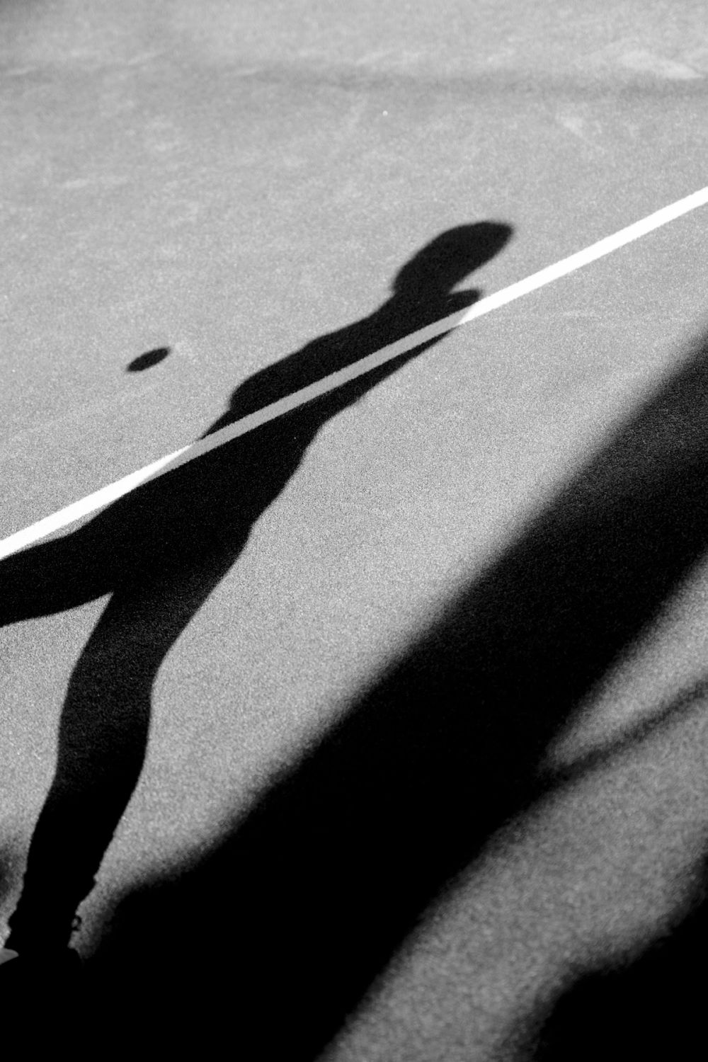 Black and white photo of shadow of a man in a padel court with a ball