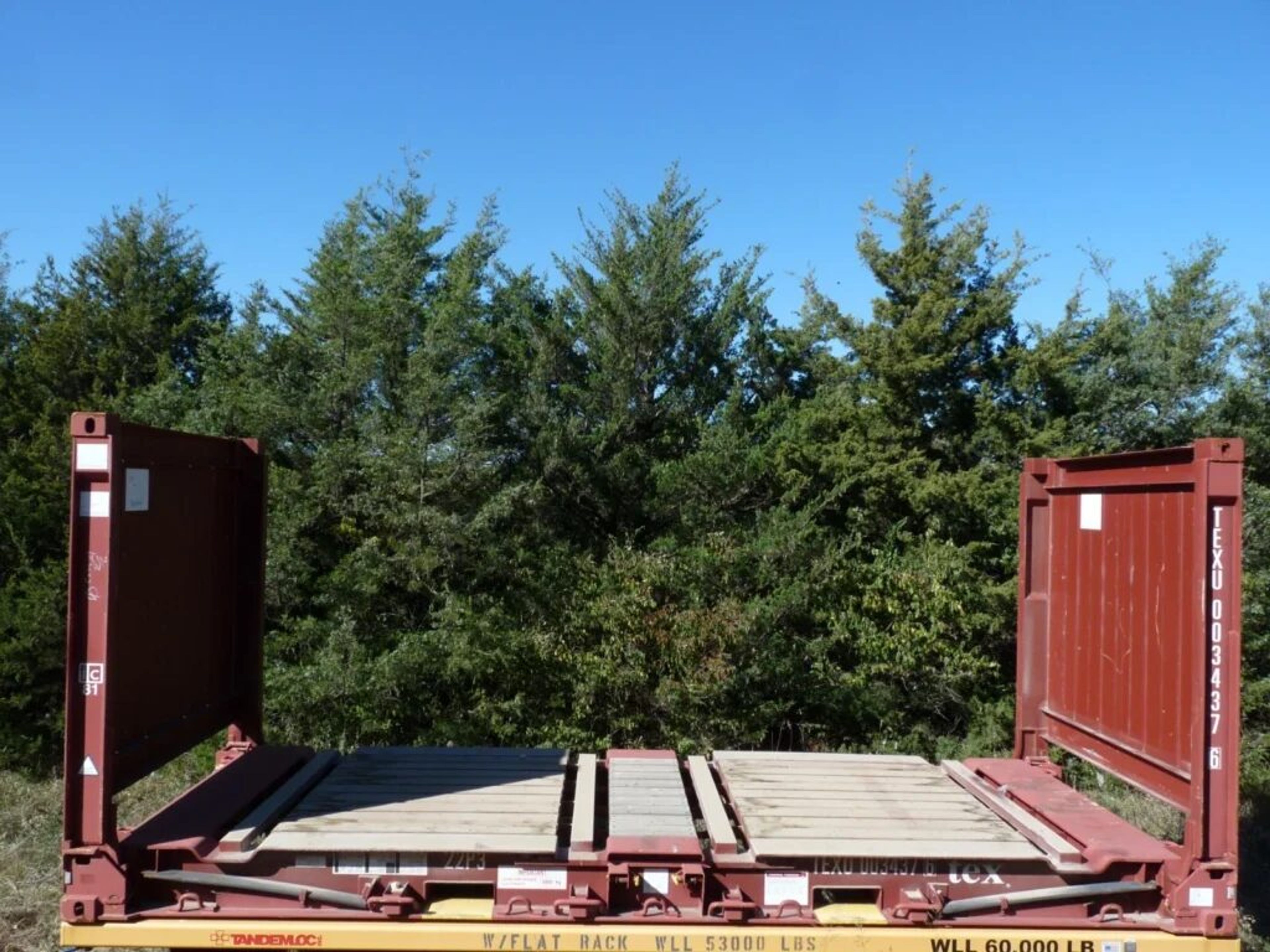 A red steel flat rack with fixed end walls and a timber deck, standing outdoors with no sides fitted