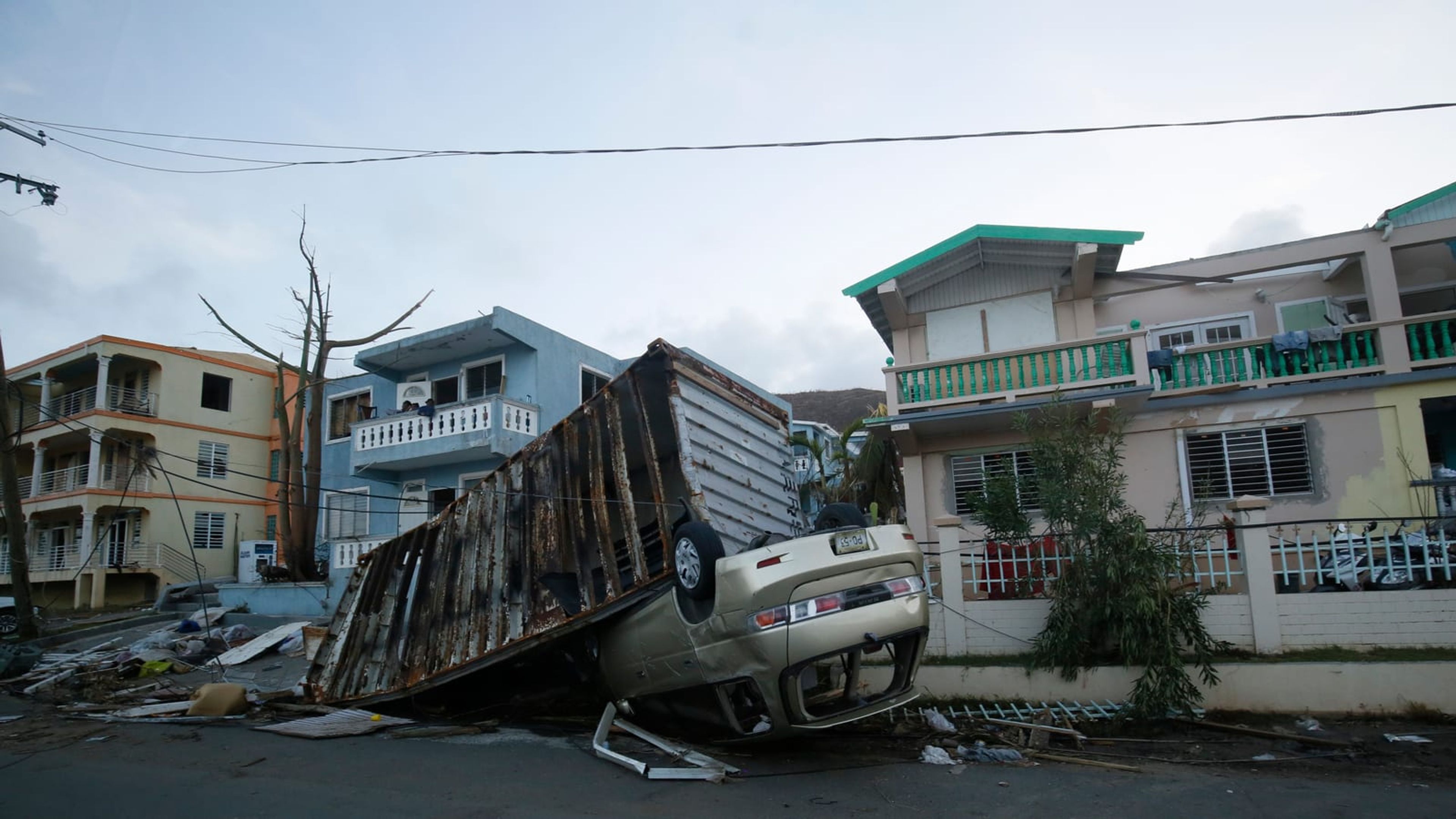 A shipping container thrown against an overturned car by hurricane winds in a residential street
