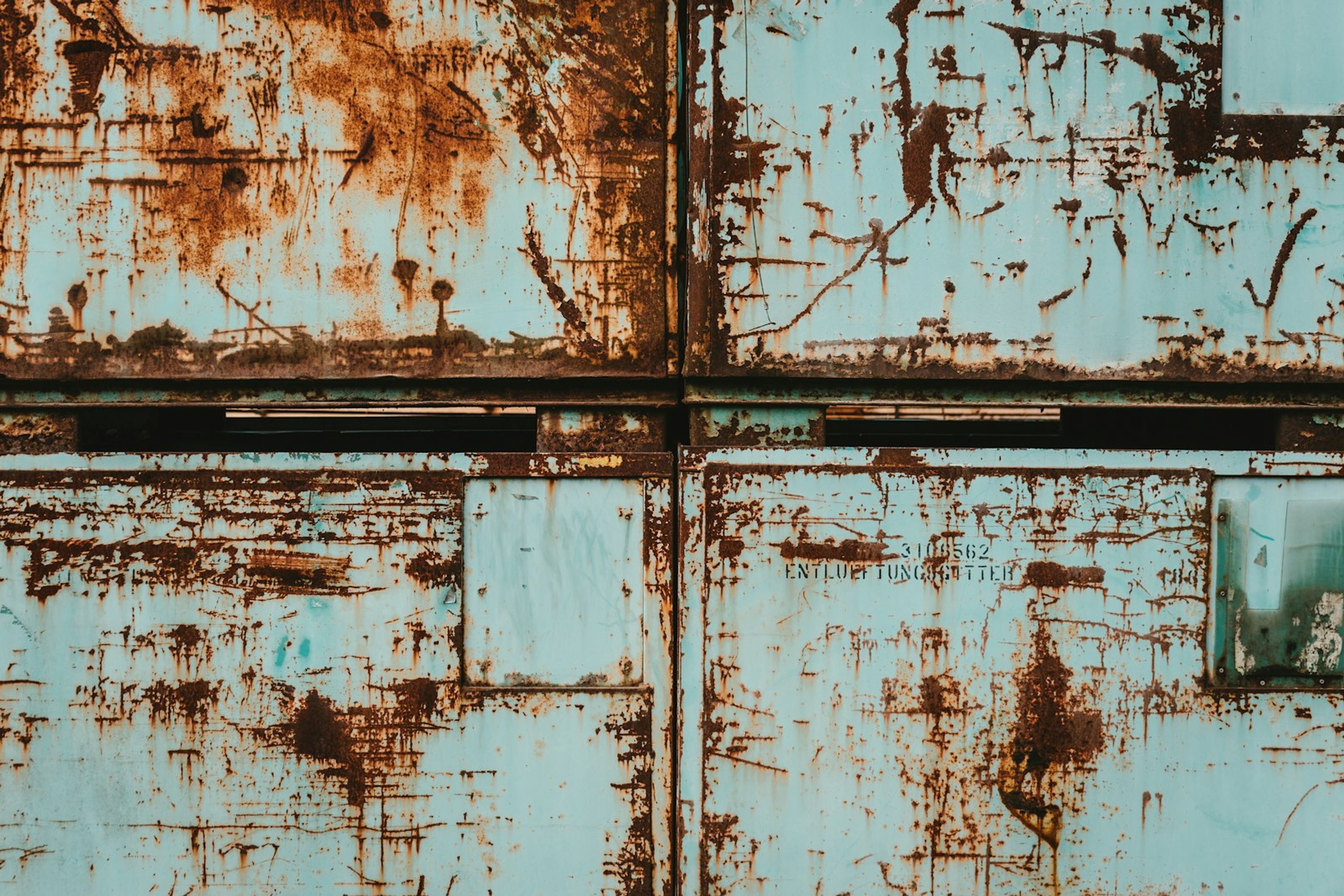 Weathered blue-green shipping container panels with chipped paint and rust streaks that need prep before repainting