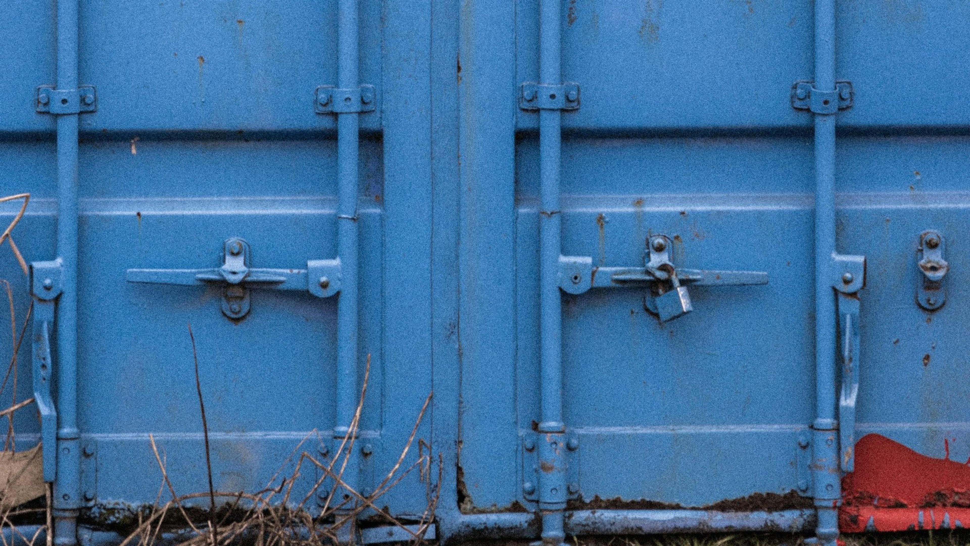 Closed blue shipping container doors showing locking bars, handles, handle retainers, and a padlock on the right door