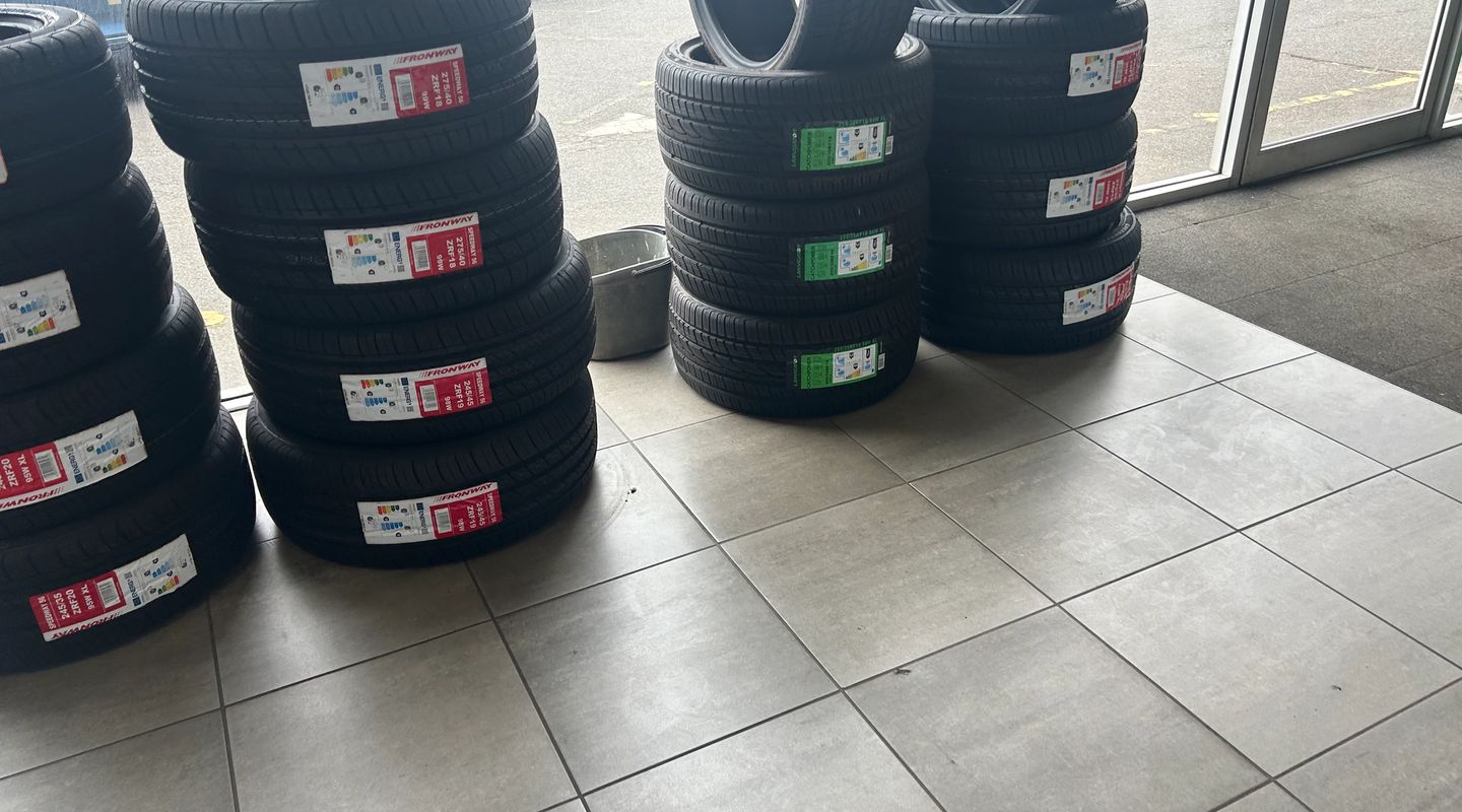 New branded tyres (Fronway and others) stacked on a garage floor, with a wet car park visible outside.