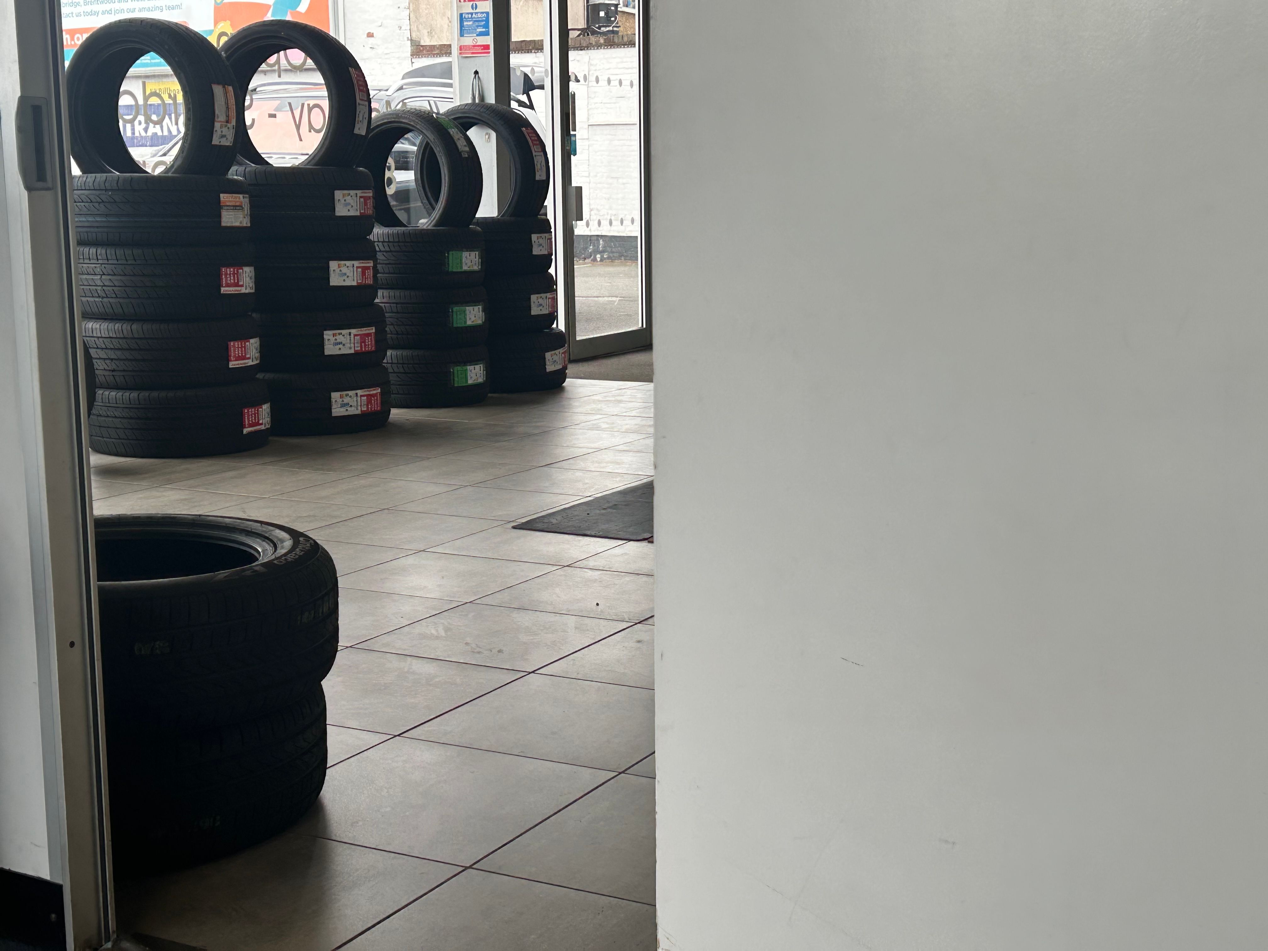 Looking through a garage doorway at stacked new tyres on a tiled floor.