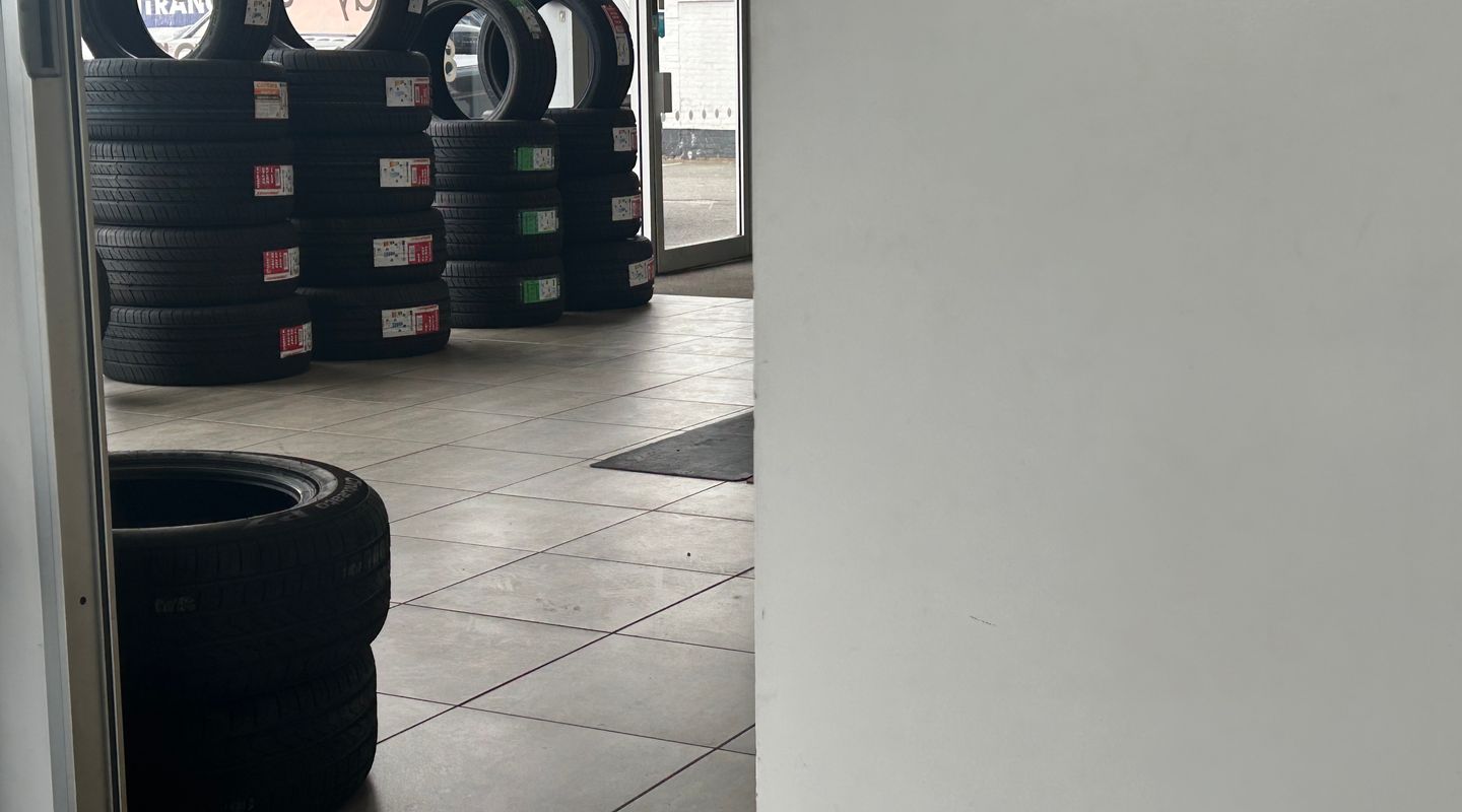 Looking through a garage doorway at stacked new tyres on a tiled floor.