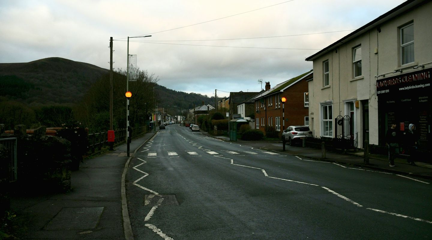 Welsh high street with a Belisha beacon (amber globe on striped pole) and white zigzag road markings at a pedestrian crossing