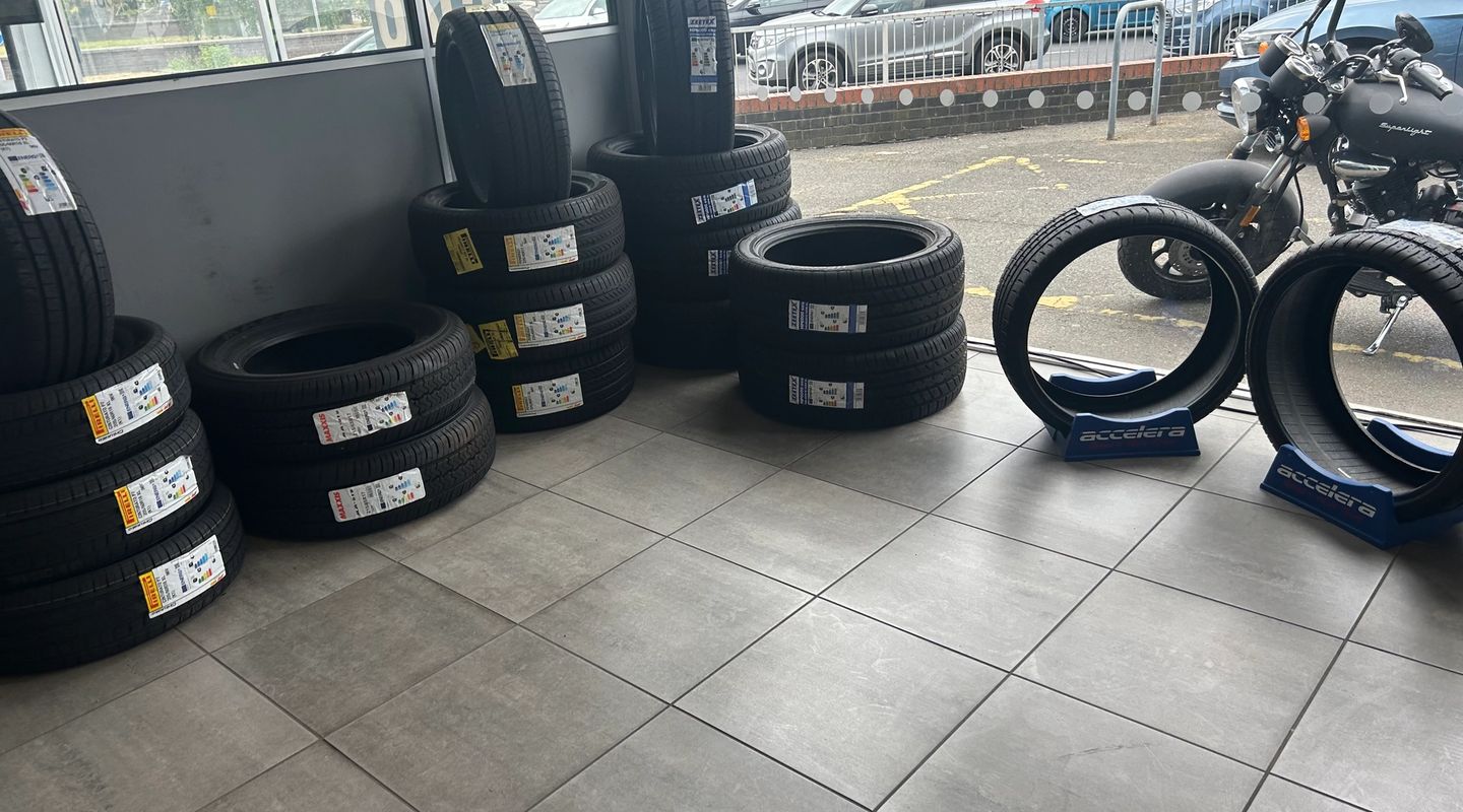 Wide shot of a tyre shop interior with branded tyre stacks, a motorcycle, and an MOT Service sign visible through the window.