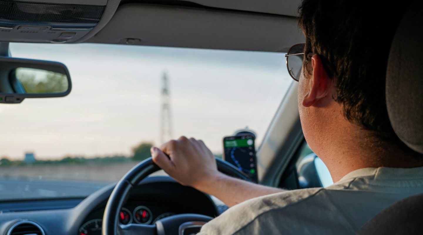 Driver wearing sunglasses at the wheel of a right-hand drive car with a phone satnav mount showing Google Maps, dusk light ou