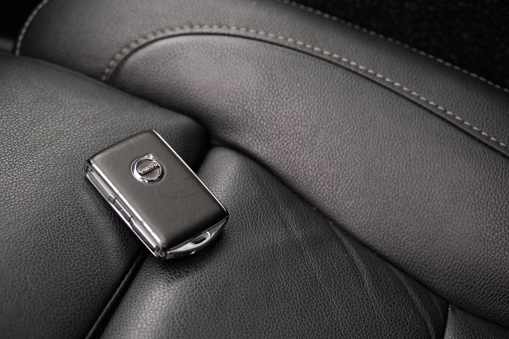 A Volvo car key fob resting on a black leather car seat, representing lending and borrowing a car.