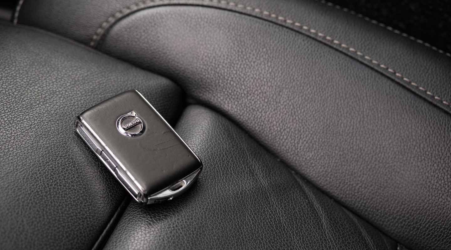 A Volvo car key fob resting on a black leather car seat, representing lending and borrowing a car.