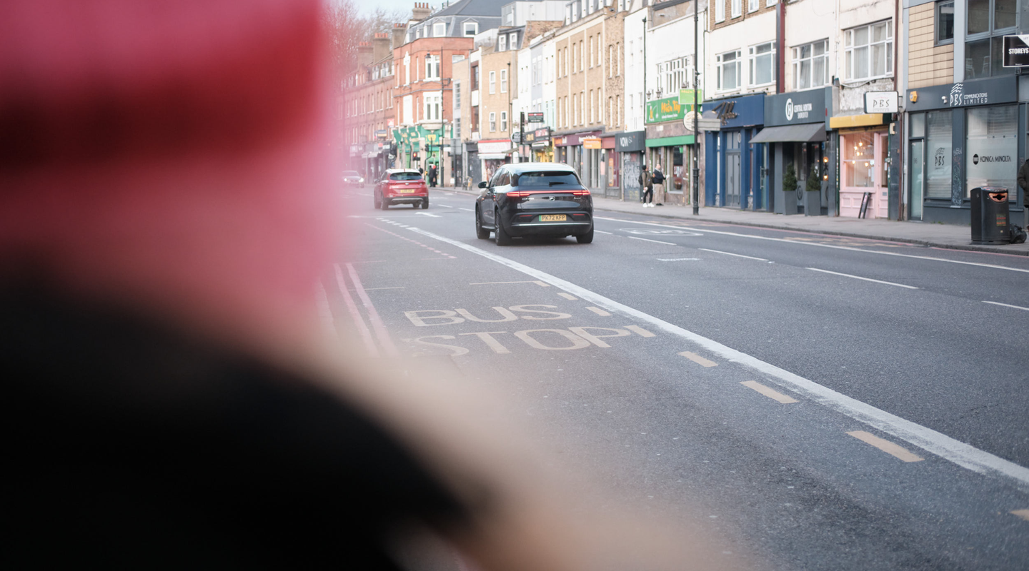 Black EV at a London bus stop with a defocused red double-decker bus in the foreground.