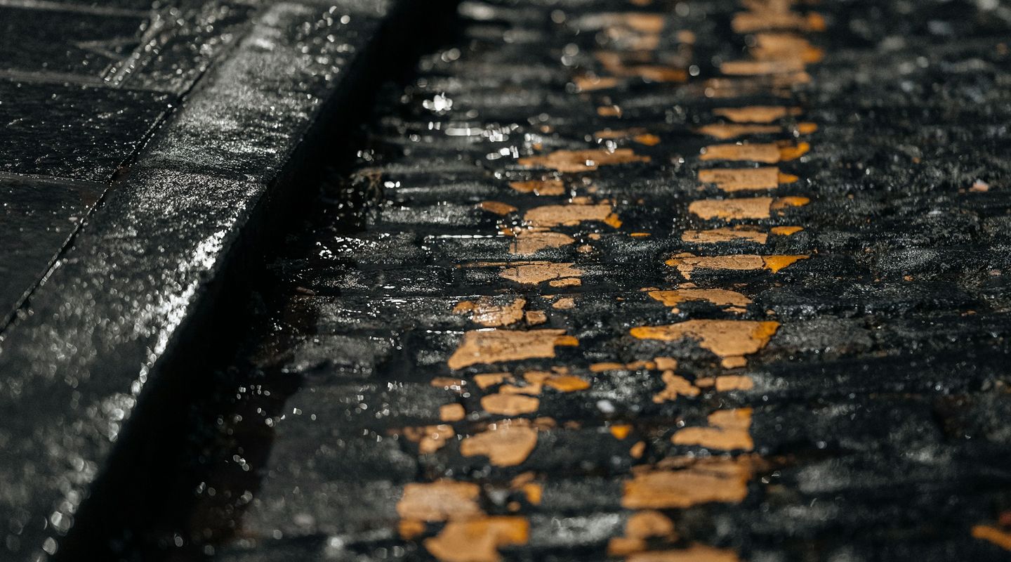 Close-up macro of wet yellow road paint on dark cobblestones at a kerb - parking signs uk