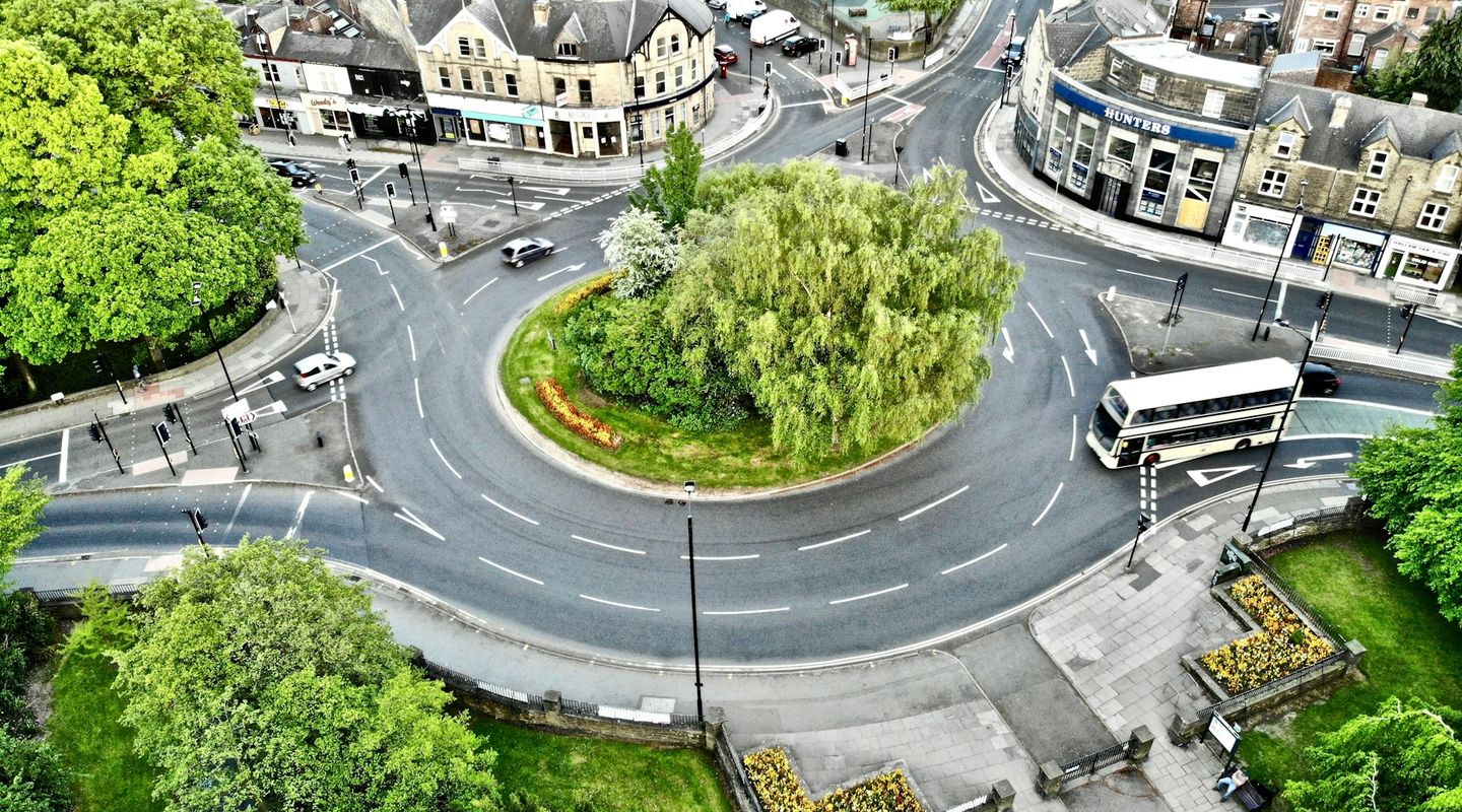 Aerial view of a UK town roundabout with a planted central island containing a willow tree - bus lanes uk