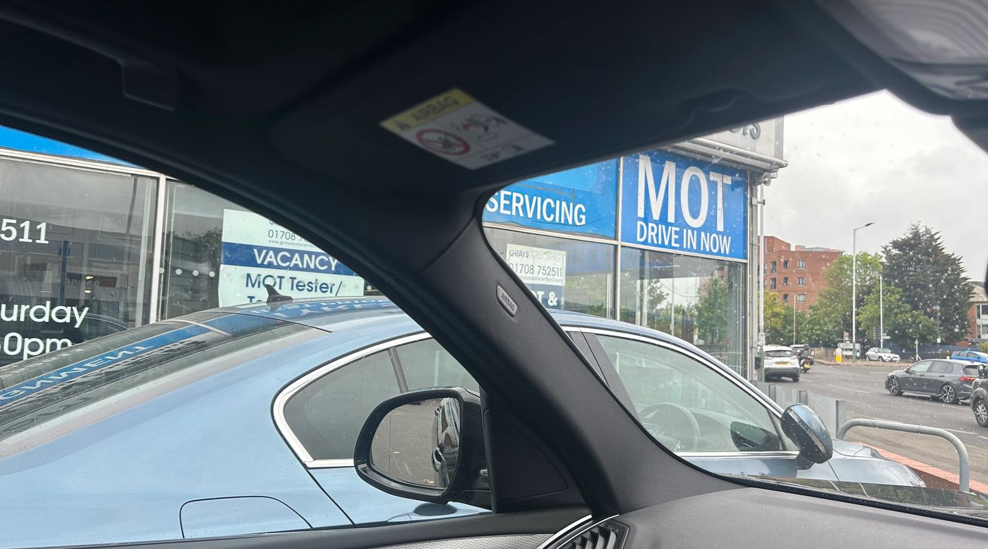 View from inside a car through the windscreen towards an MOT DRIVE IN NOW sign on a garage forecourt.