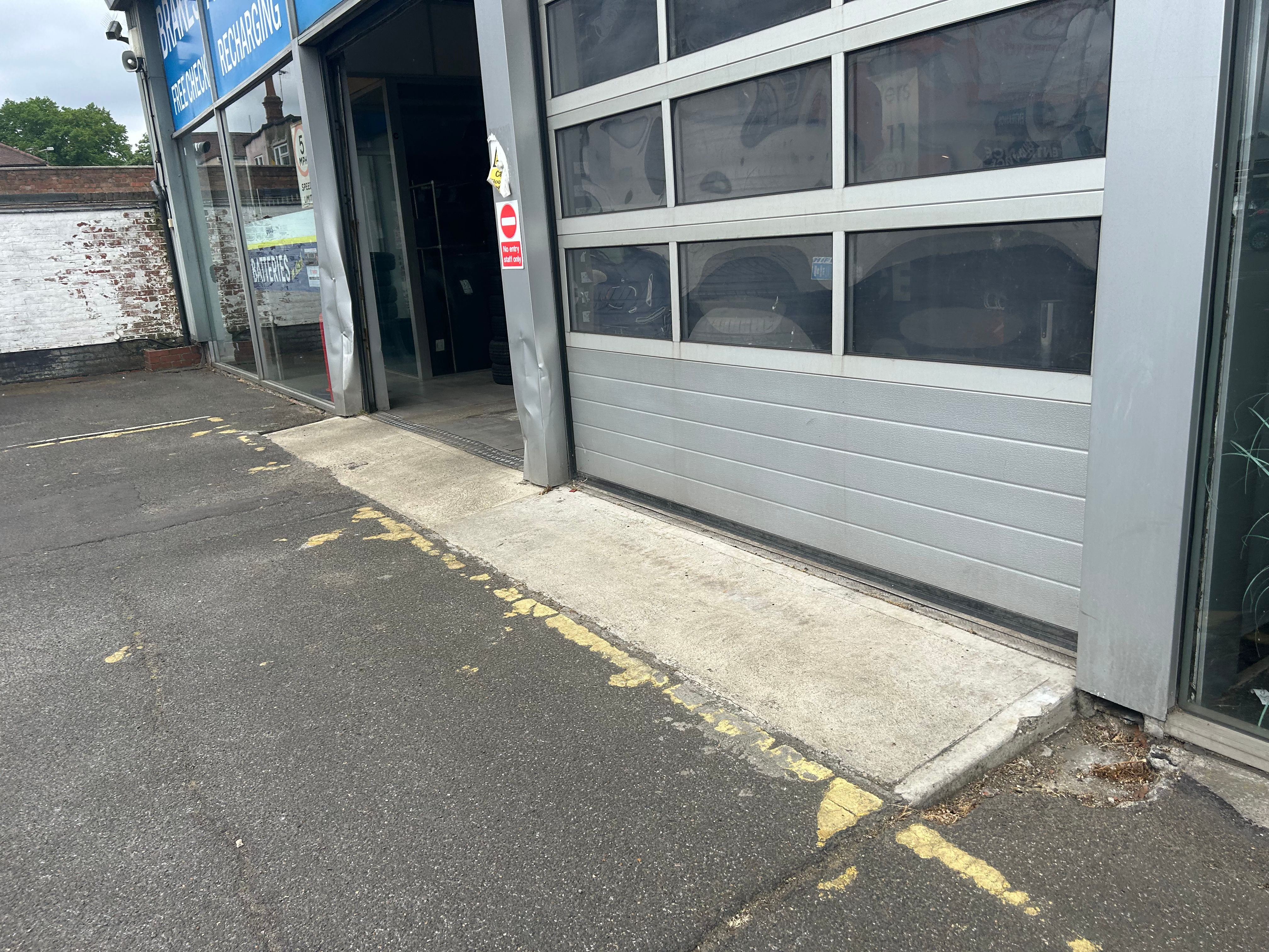 Garage exterior with roller doors partially open, yellow lines on the forecourt.