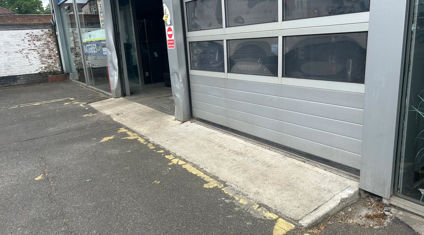 Garage exterior with roller doors partially open, yellow lines on the forecourt.