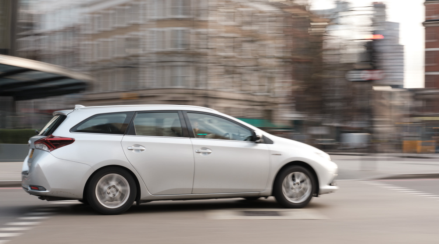 Panning shot of a silver estate moving through a central London street, blurred period buildings behind.