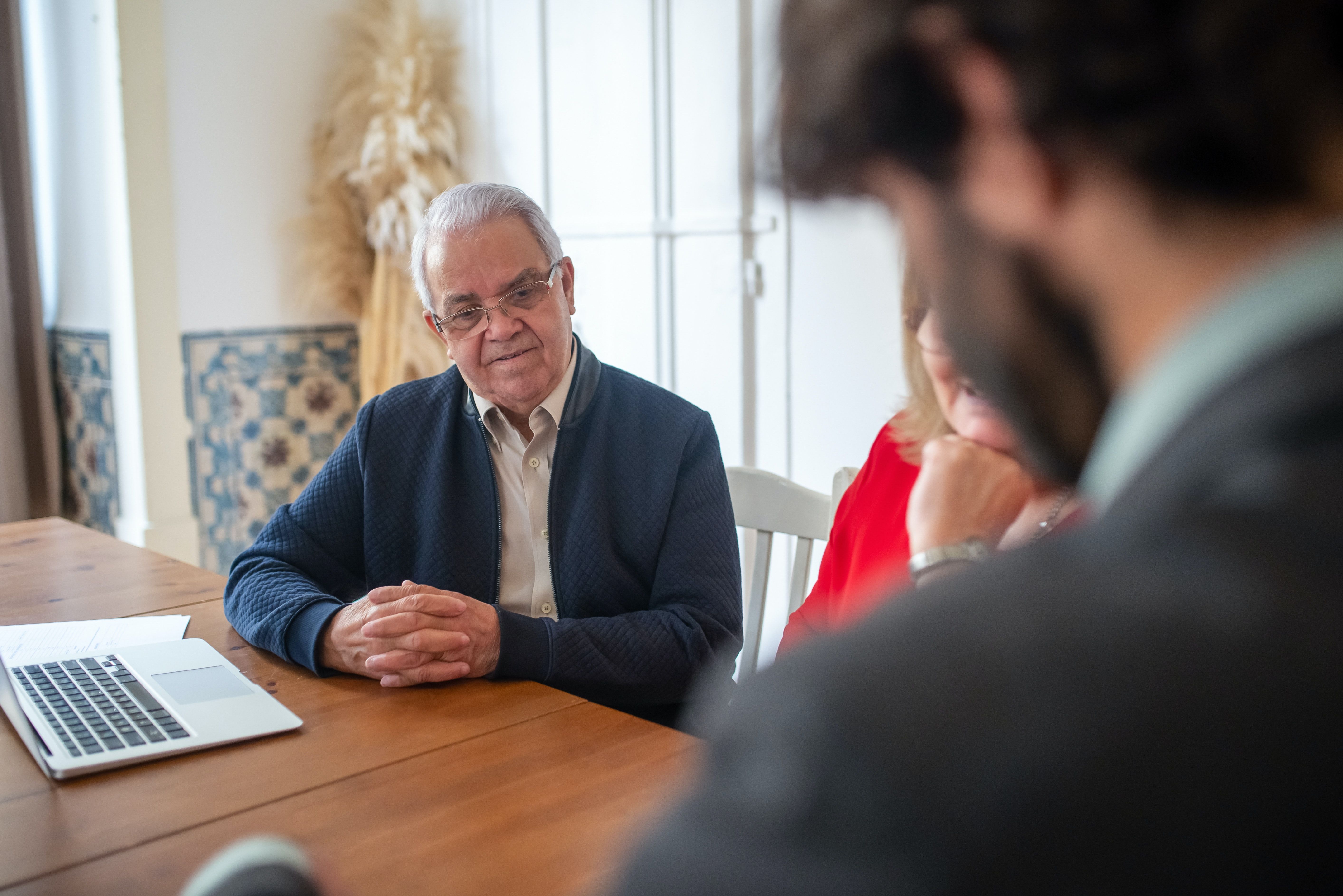 An older couple meets with a bearded financial advisor at a wooden desk.