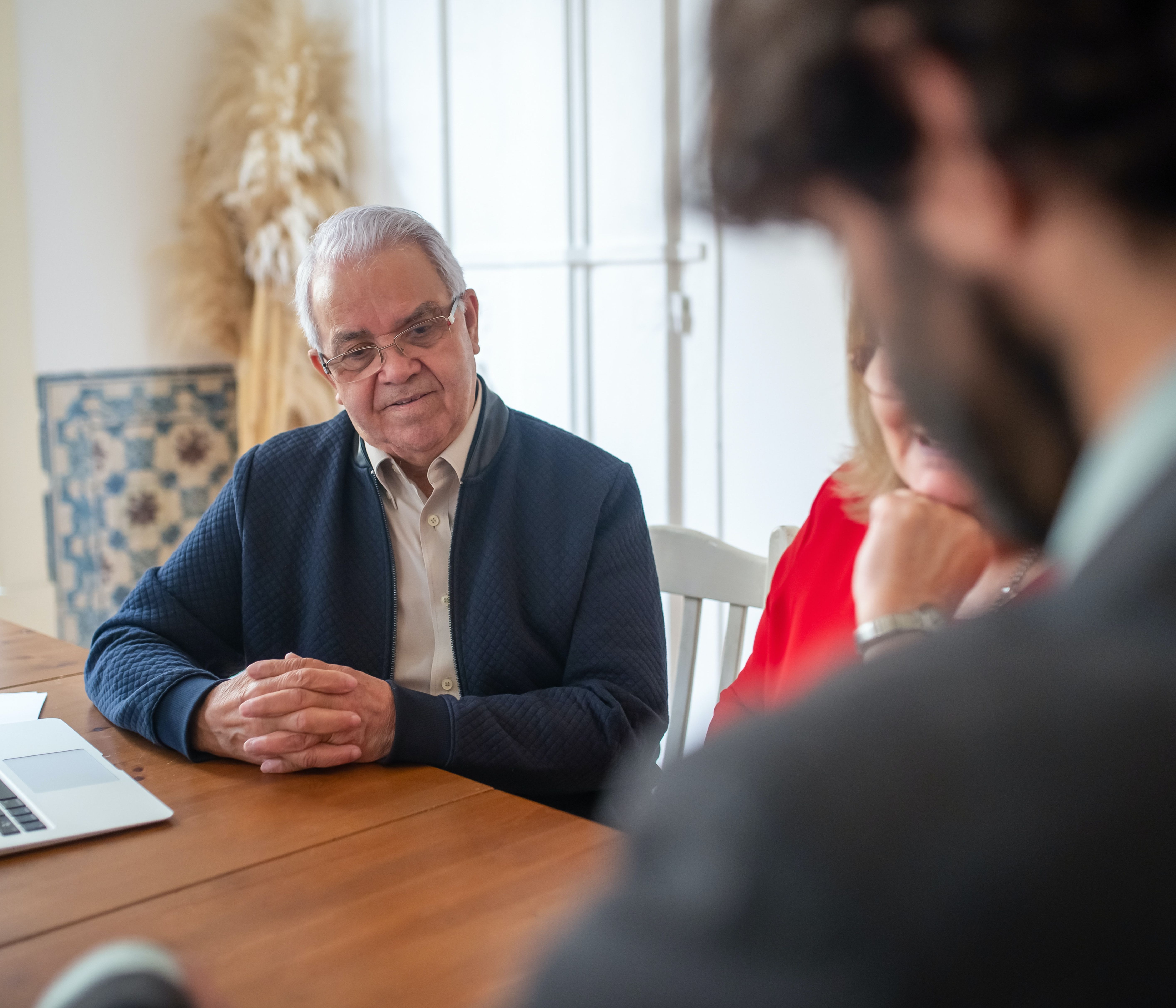 An older couple meets with a bearded financial advisor at a wooden desk.