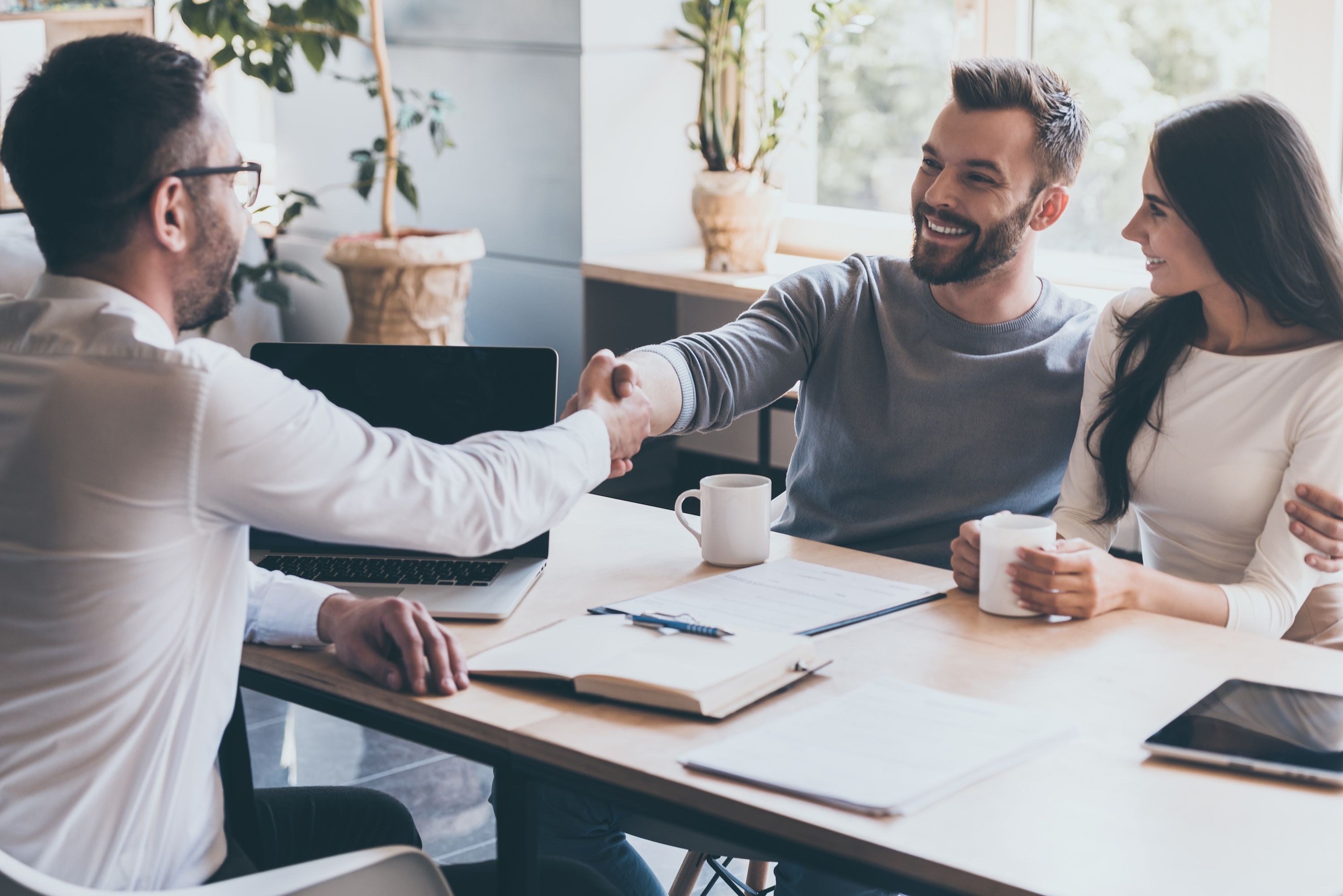 A financial advisor shakes hands with a man during a meeting with a couple.