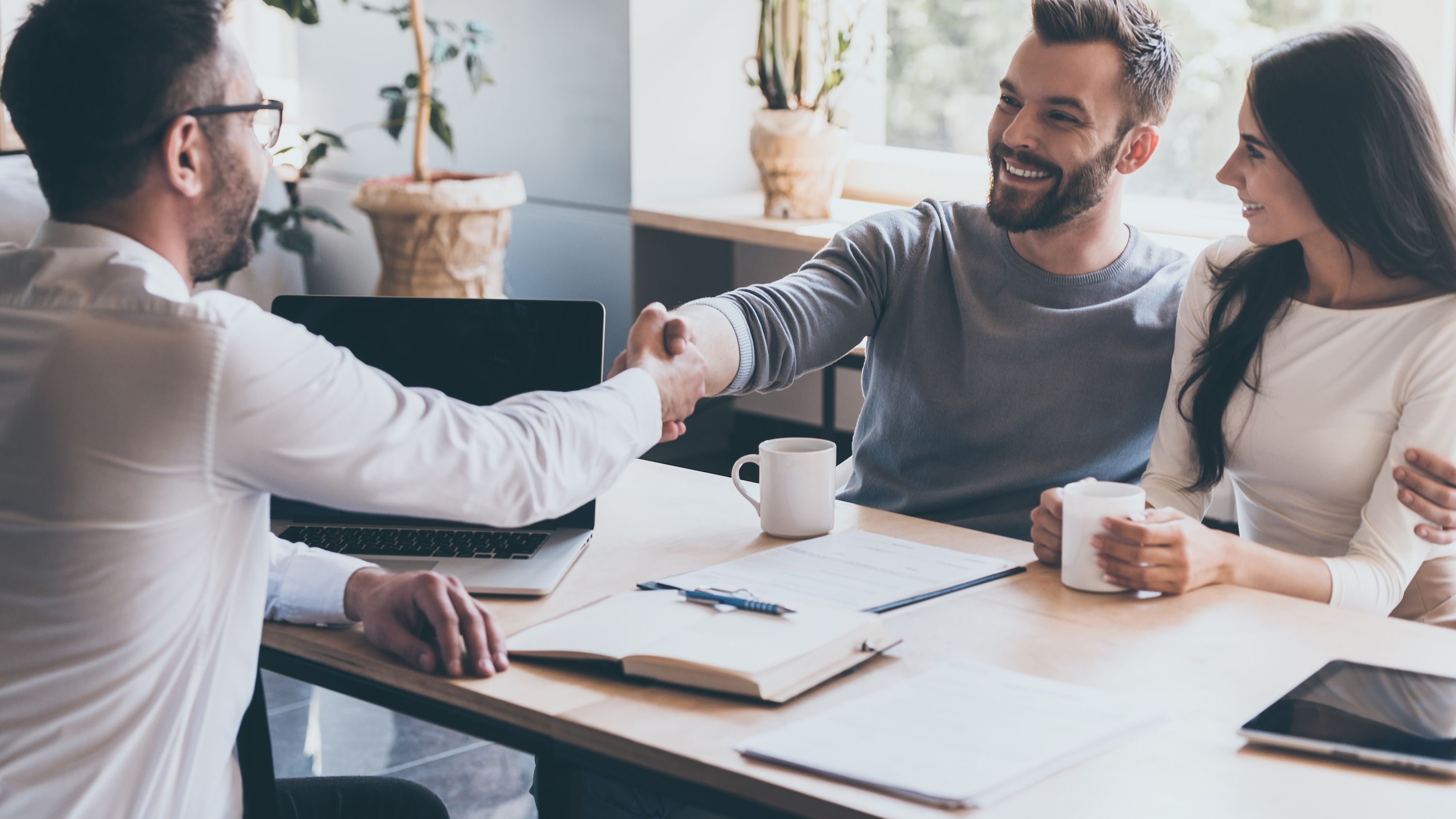 A financial advisor shakes hands with a man during a meeting with a couple.