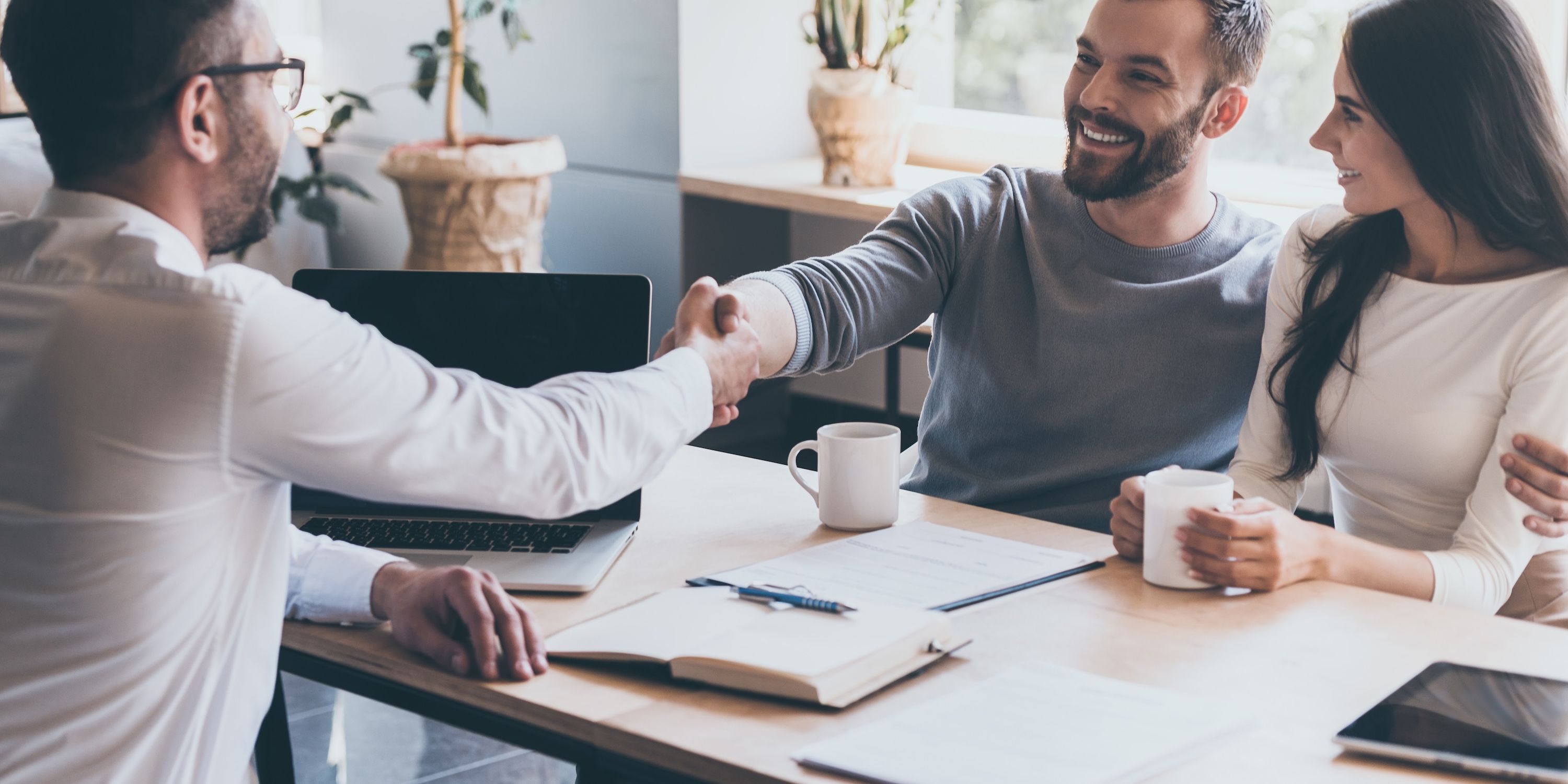 A financial advisor shakes hands with a man during a meeting with a couple.