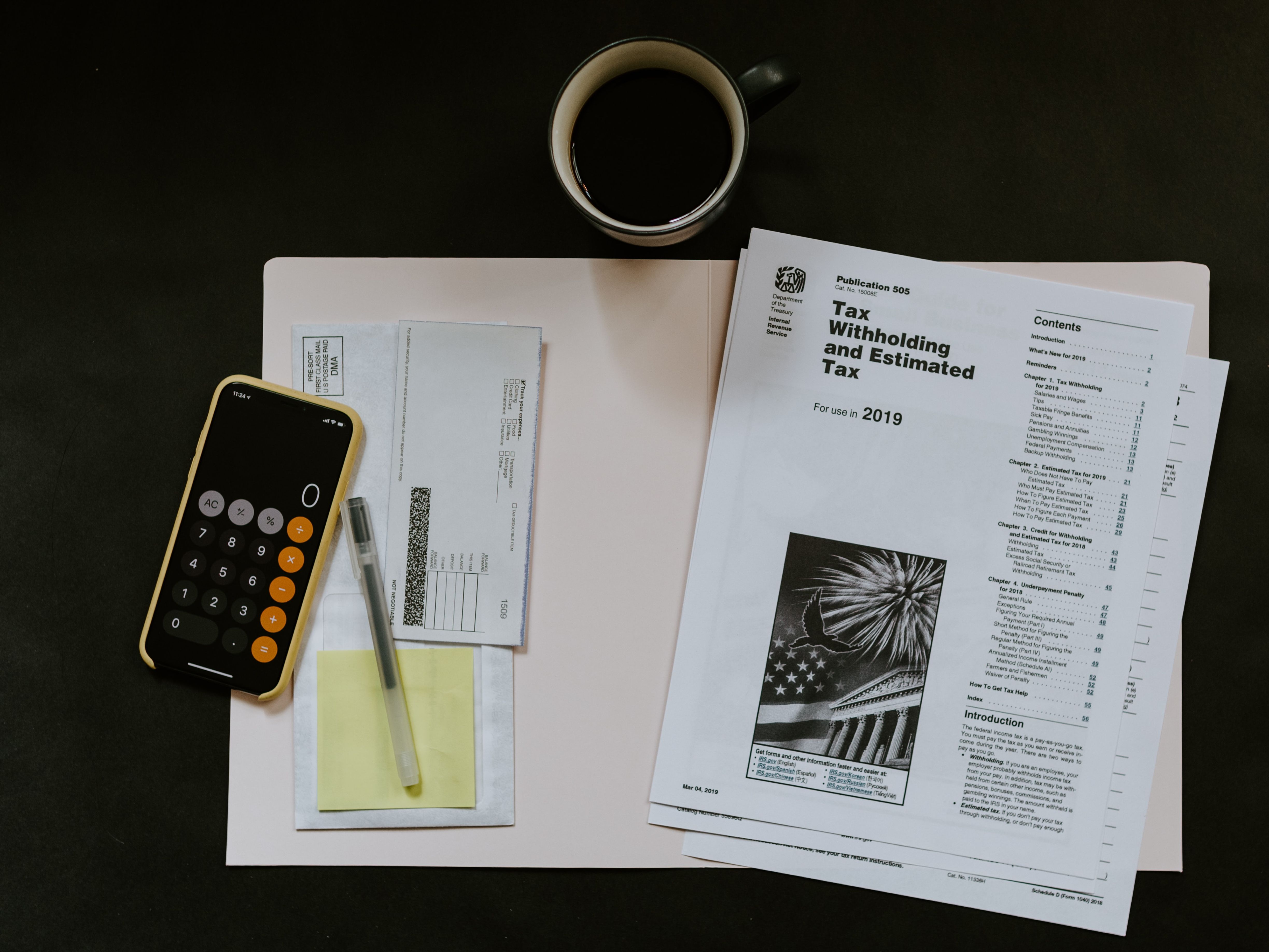 Tax files, a calculator and a filing folder sit near a cup of black coffee.