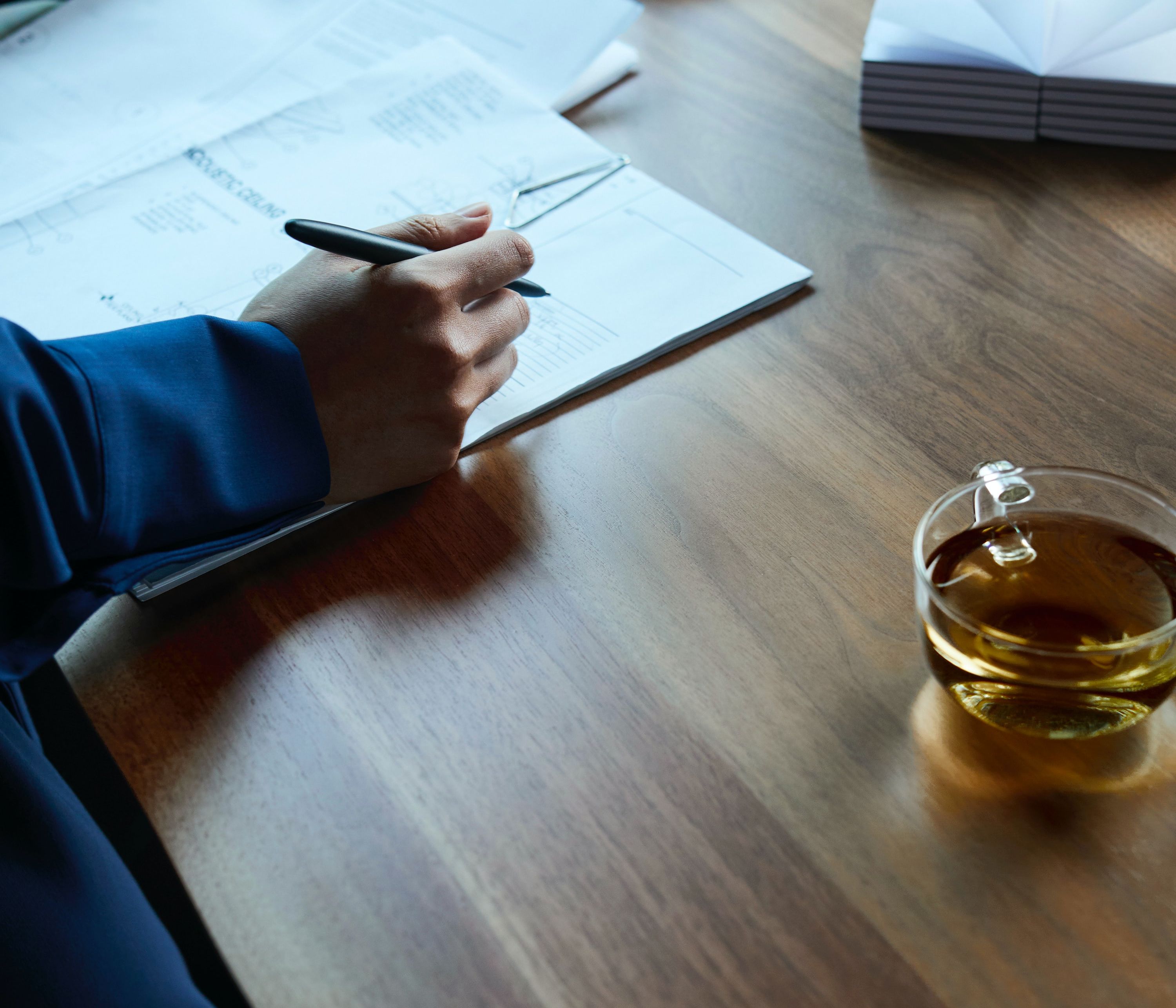 A person files their taxes next to a cup of tea in a clear cup.