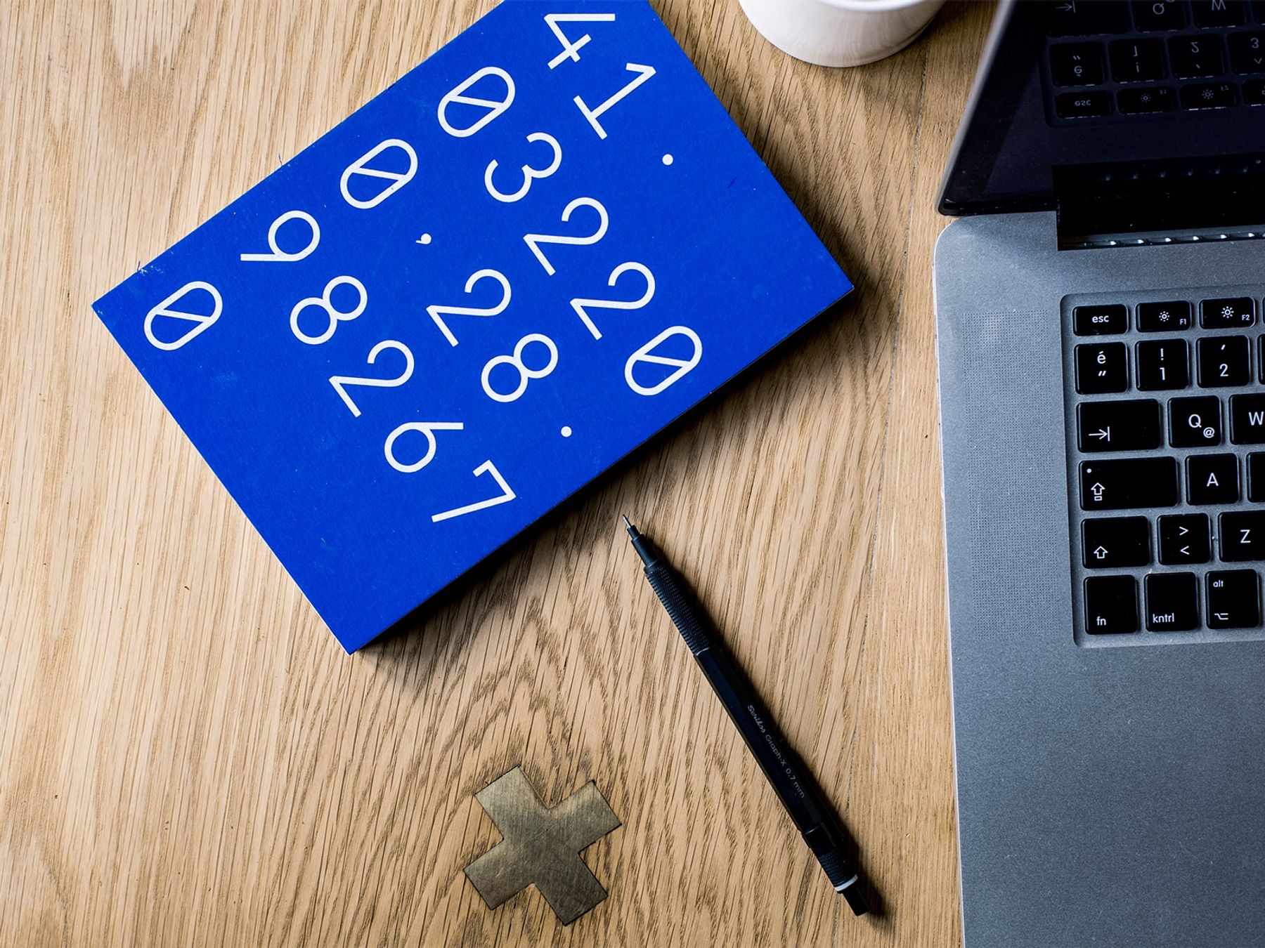 A bright blue notebook with numbers on it, lying adjacent to a pen and laptop.