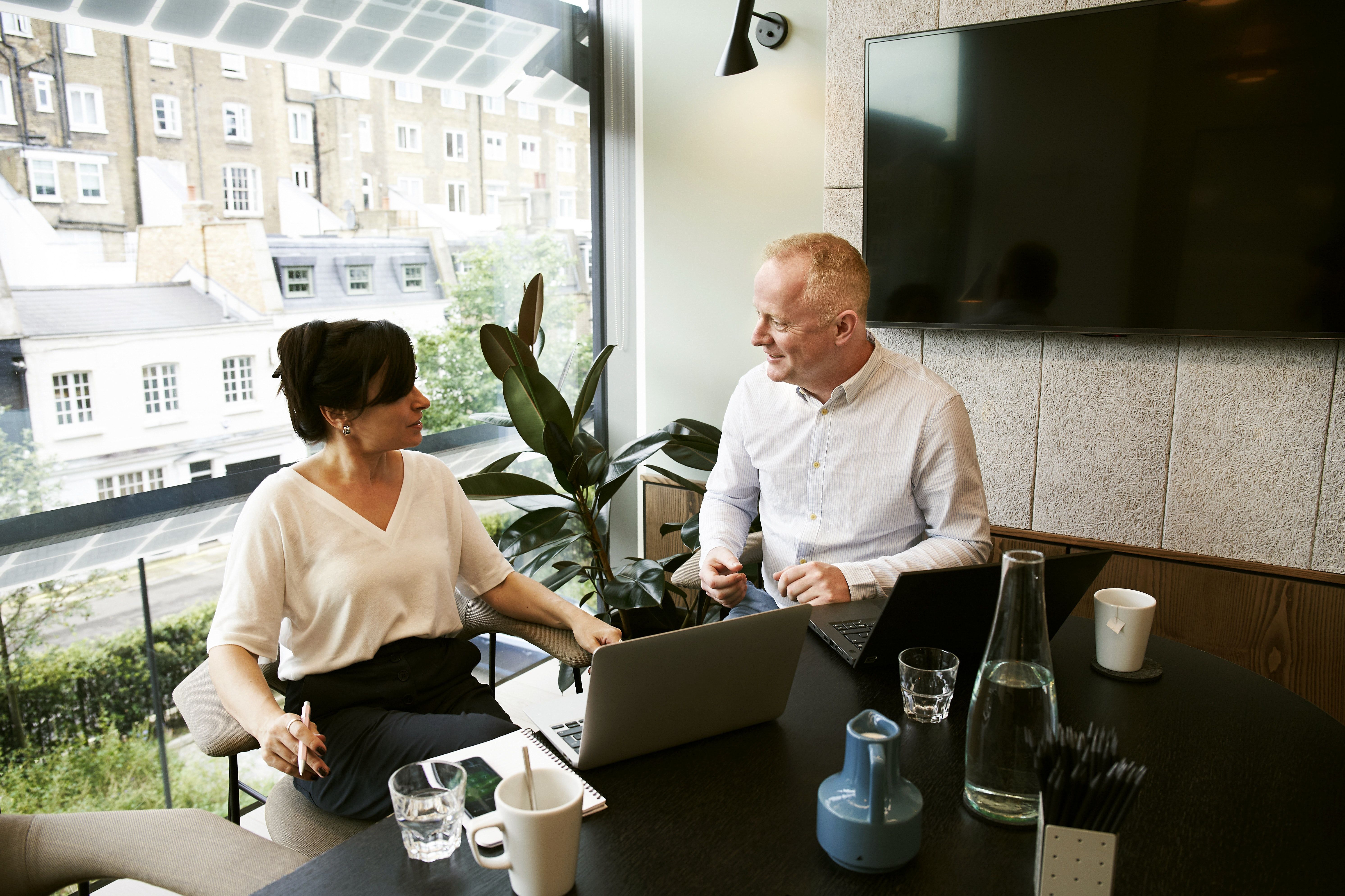 An accounting professional and a client meet at a dark desk near a bright window to discuss business matters.