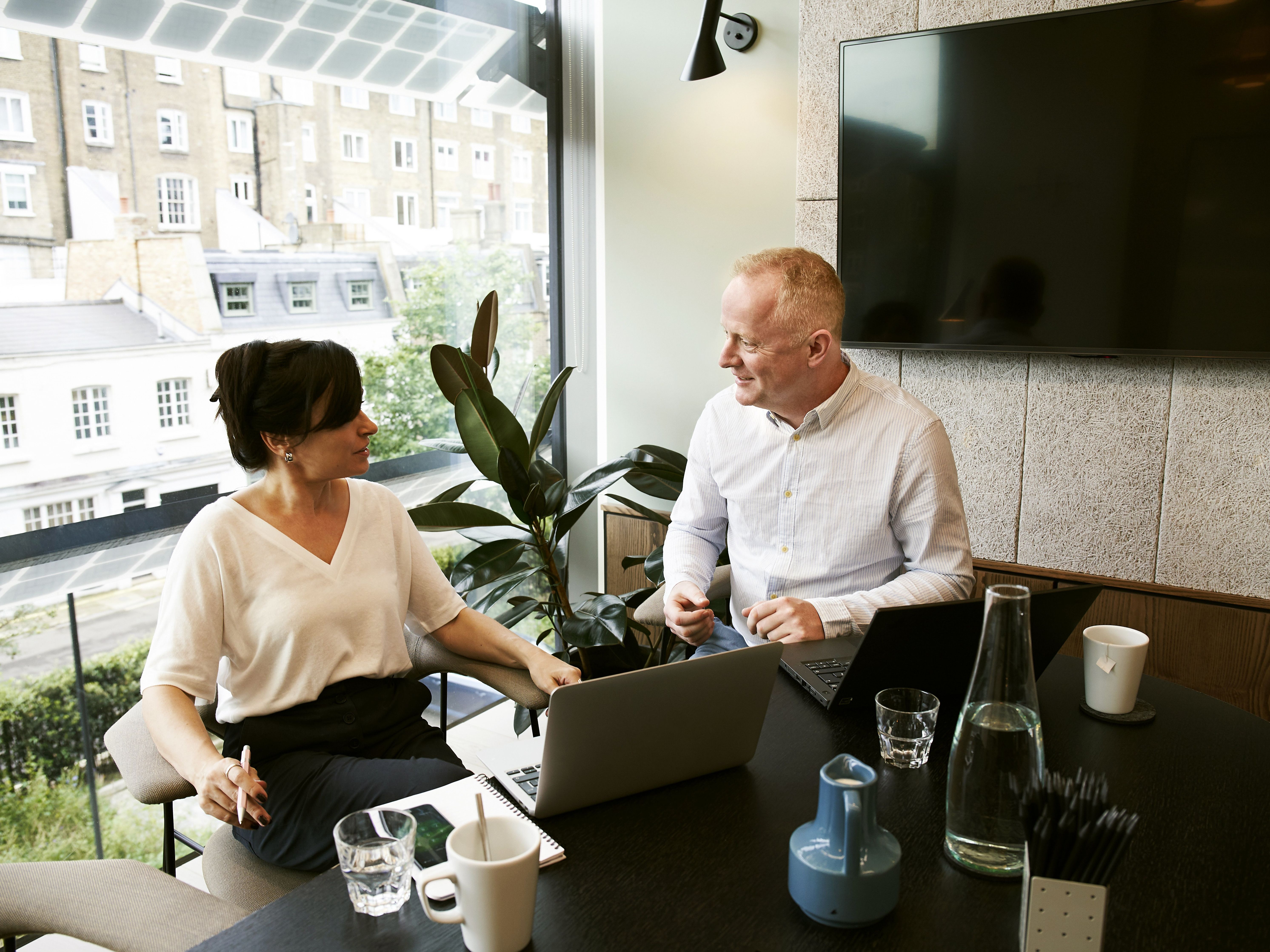 An accounting professional and a client meet at a dark desk near a bright window to discuss business matters.